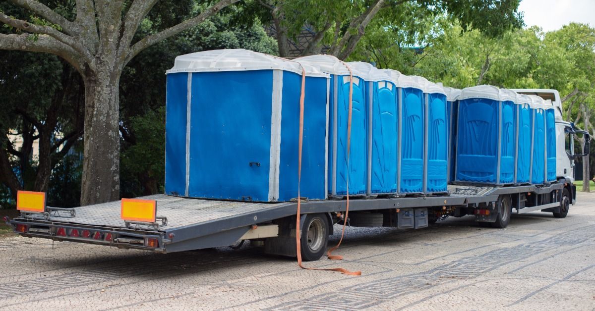 An inventory of blue portable restroom units sit on a truck bed. The truck is getting ready to unload the units.