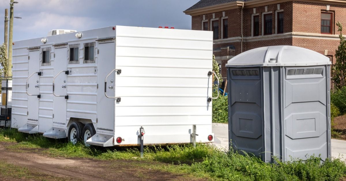 A small row of porta potties sits outside at a jobsite. The gray unit is standard and the white units are ADA-compliant.