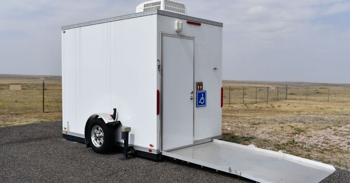 A white, hitch-style restroom trailer with an on-ramp for ADA accessibility.