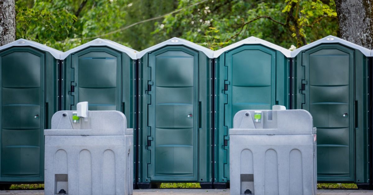 A row of five green portable toilets sit together in the park at an event.