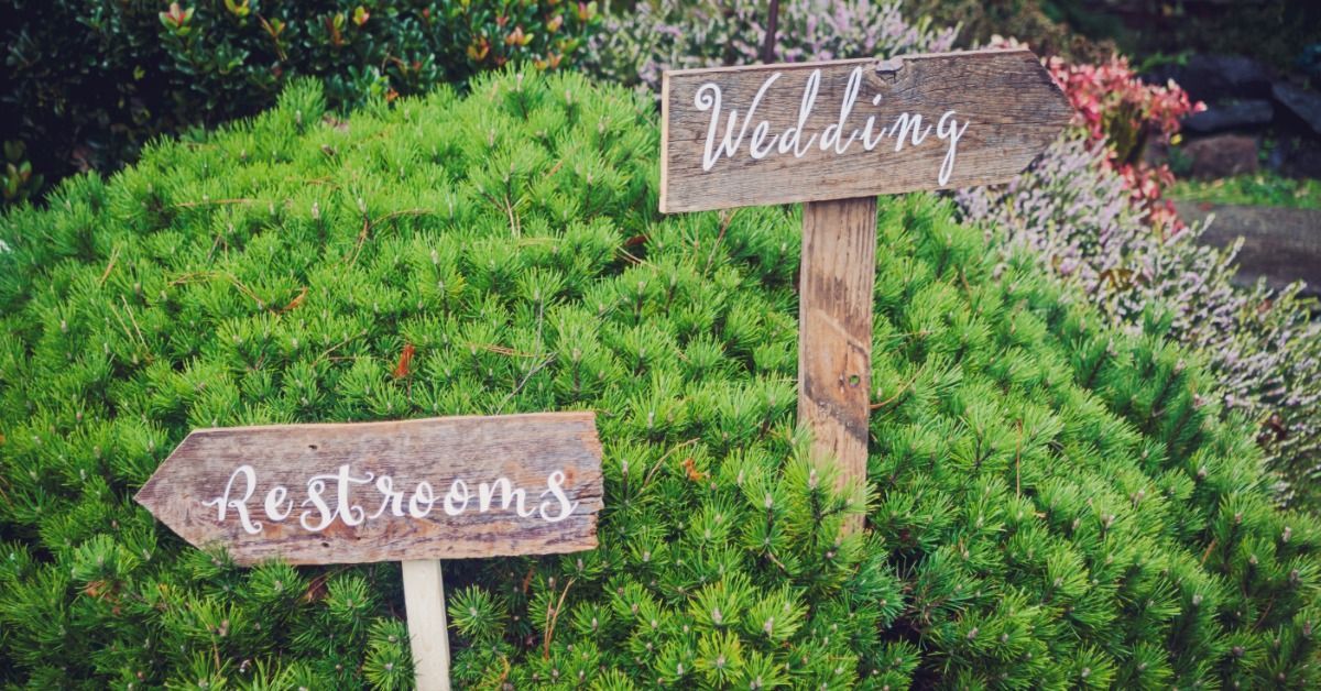 A bush at an outdoor wedding with rustic, wooden yard signs signaling the wedding and restroom locations.