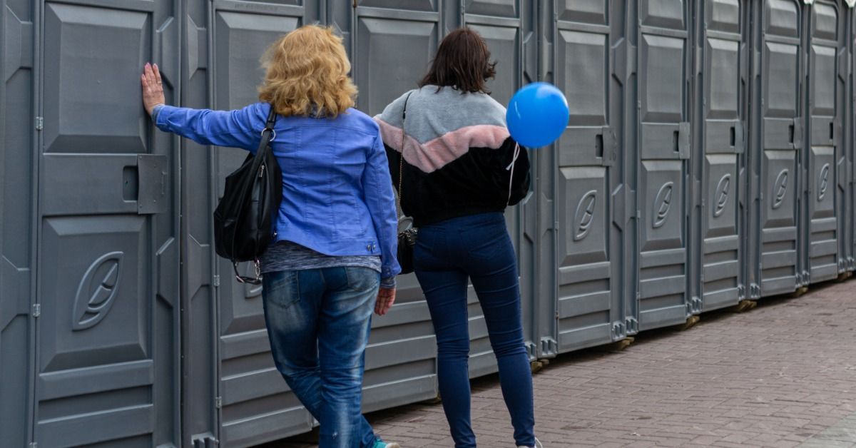 Two event attendees stand next to the line of portable restroom rentals. The restroom units are gray
