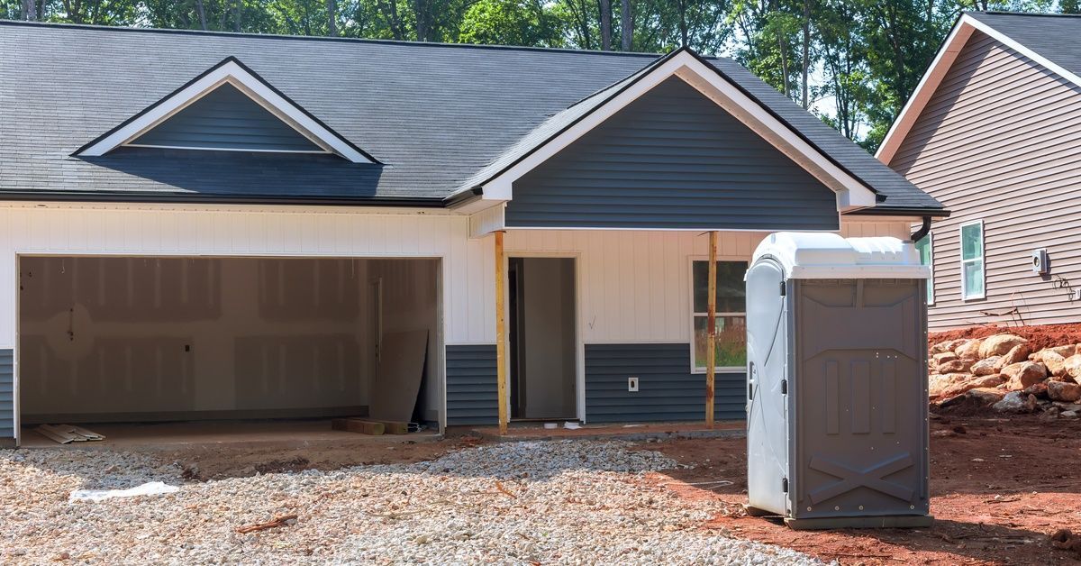 A new home build with the garage door open and a freshly maintained portable toilet unit sitting in the front yard.