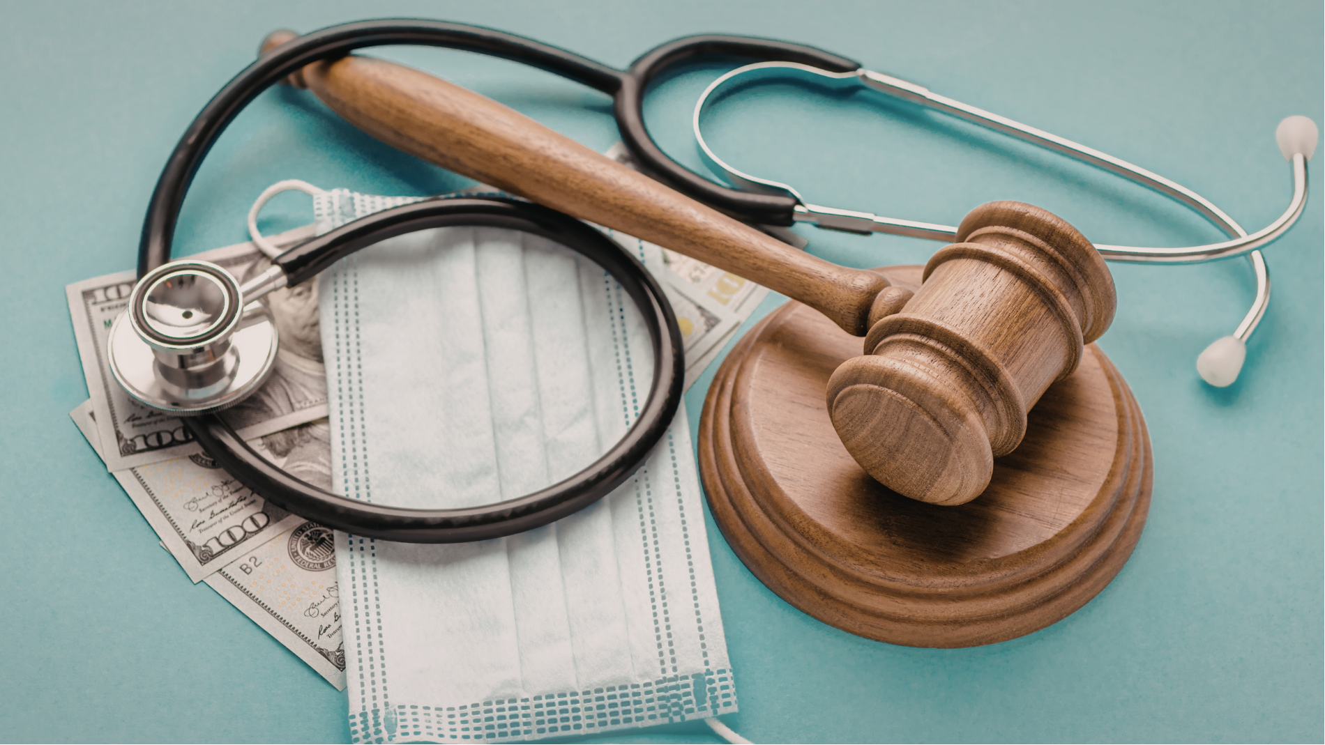 Stethoscope, face mask, and gavel on a teal surface, symbolizing healthcare law or medical justice