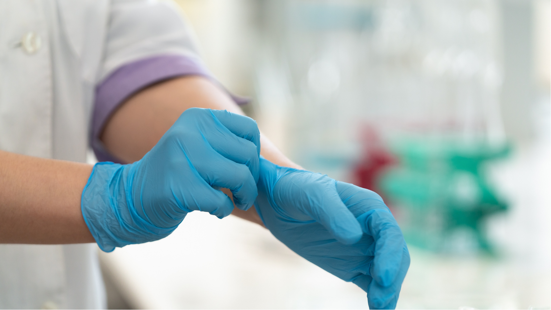 Blue-gloved hands pulling on a medical glove in a clinical setting