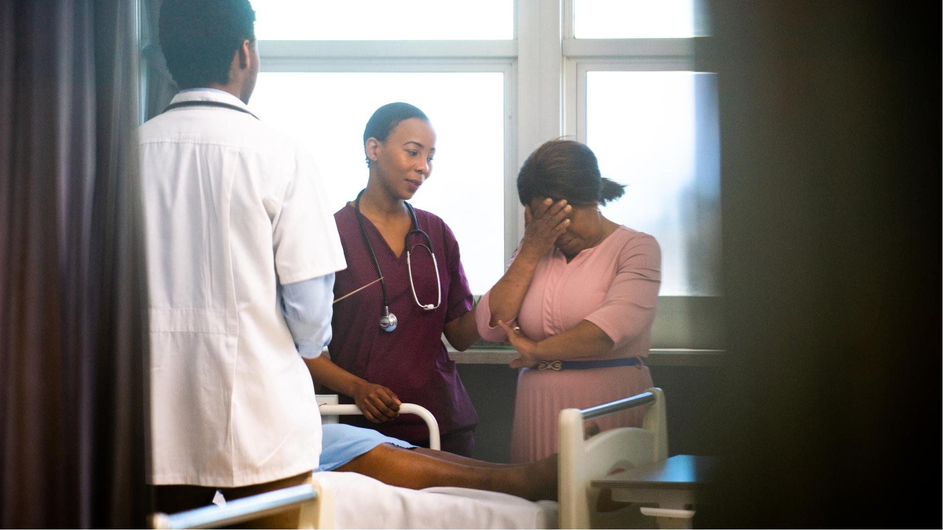 Doctor and nurse talking with a concerned patient beside a hospital bed in a bright room