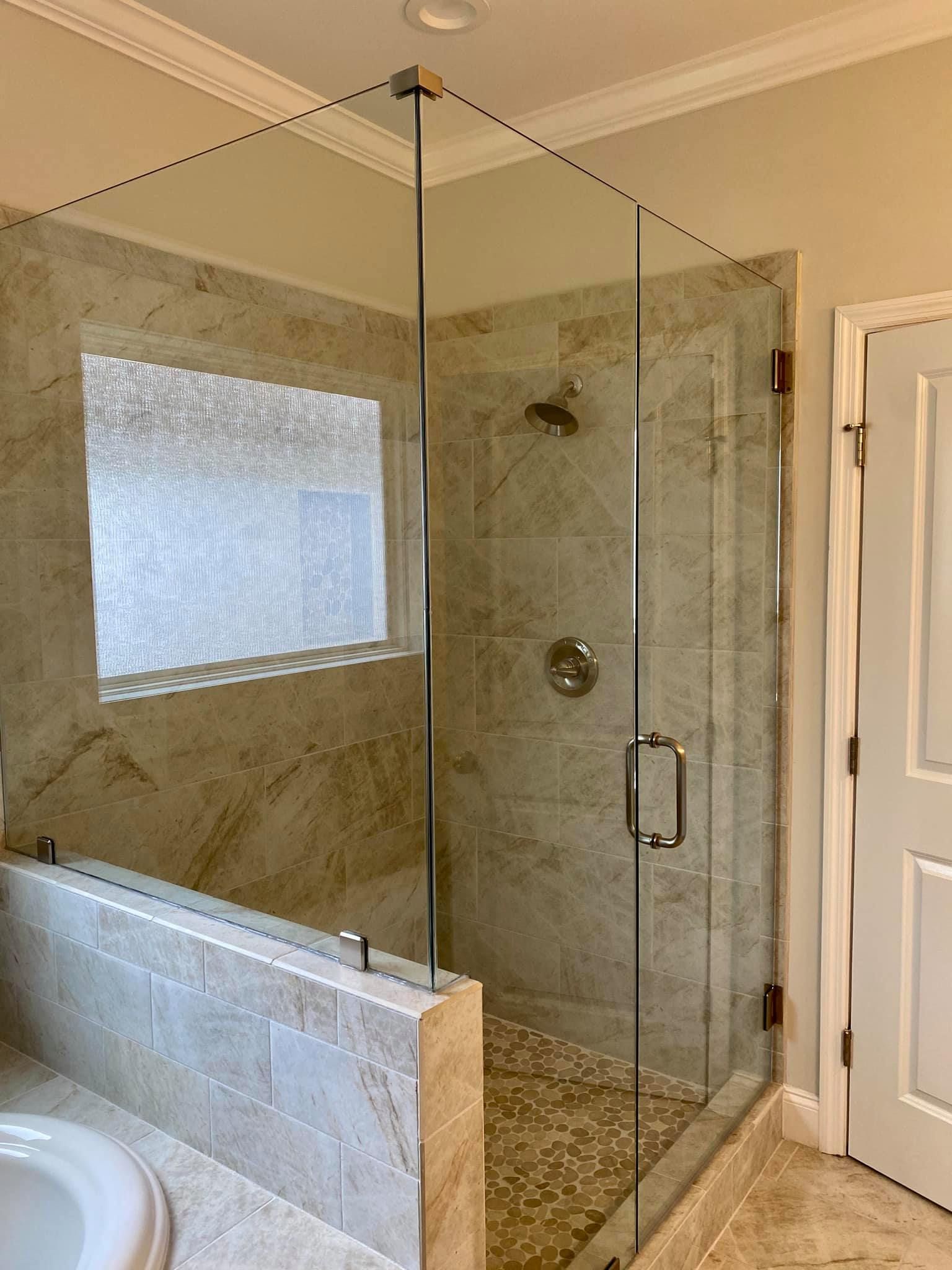 Glass shower enclosure with pebbled floor, beige tile walls, and chrome fixtures.