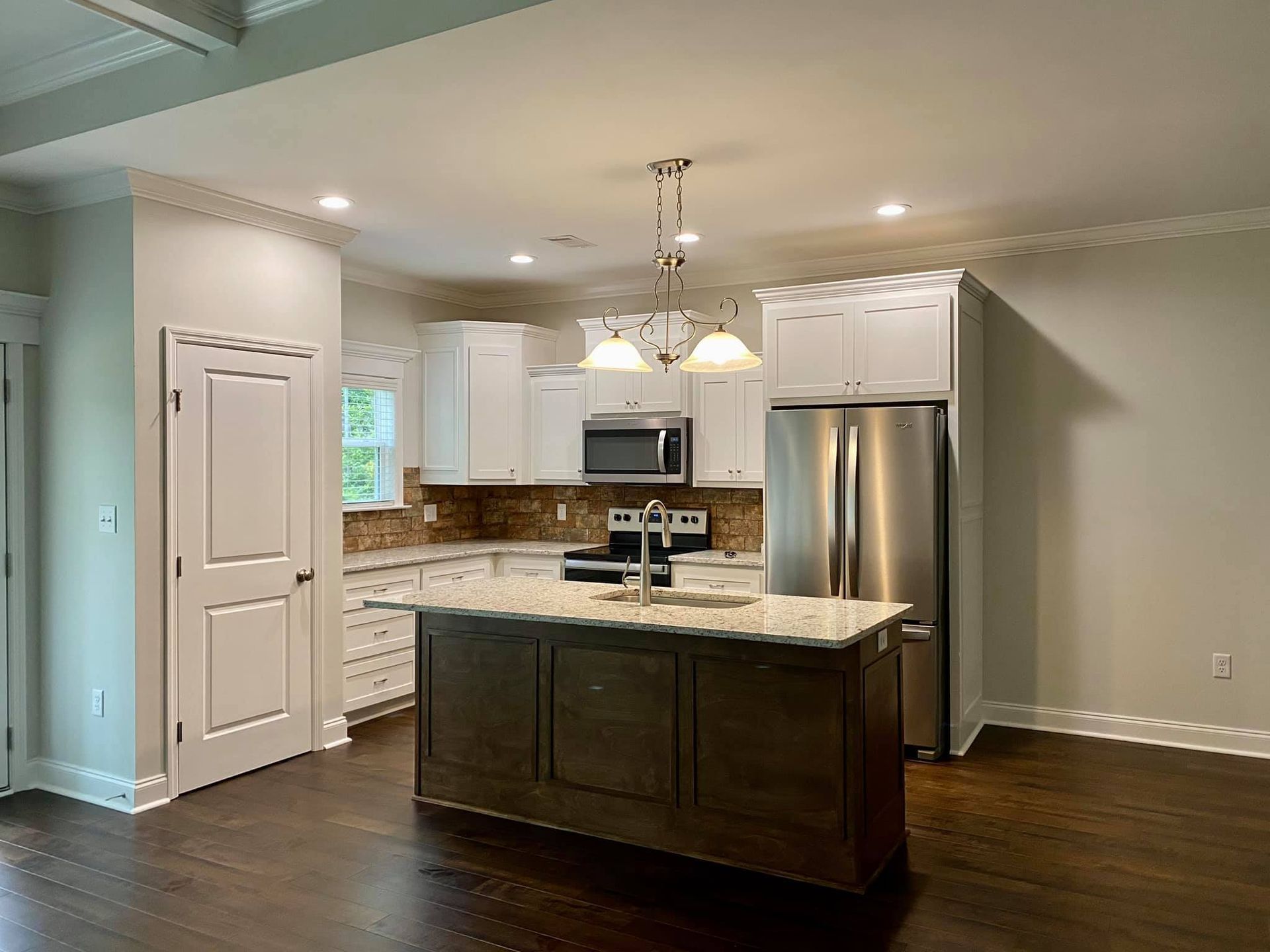 Modern kitchen with white cabinets, stainless steel appliances, dark wood island, and granite countertops.
