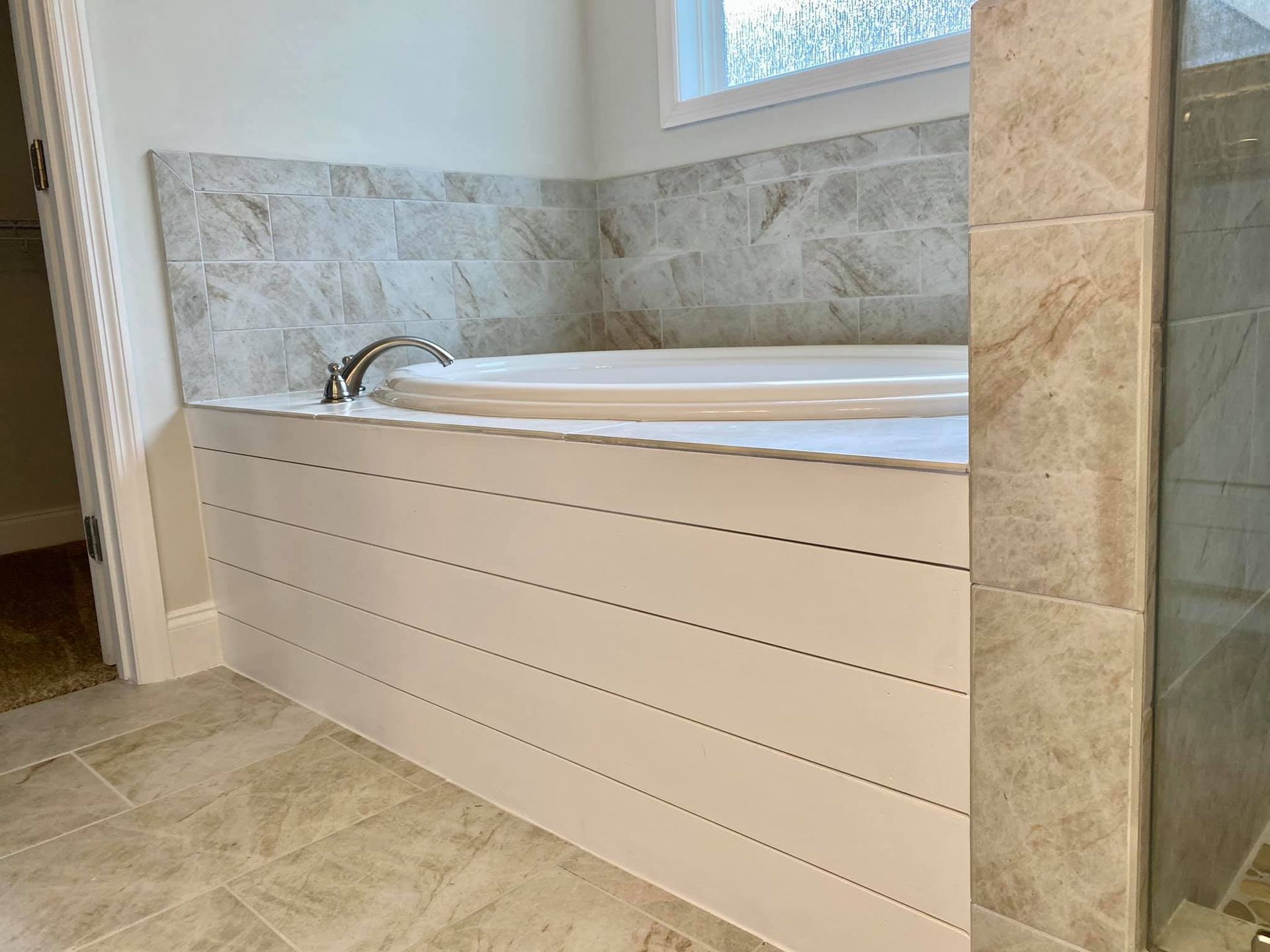 White bathtub with silver faucet, surrounded by tile and white paneling in a bathroom.