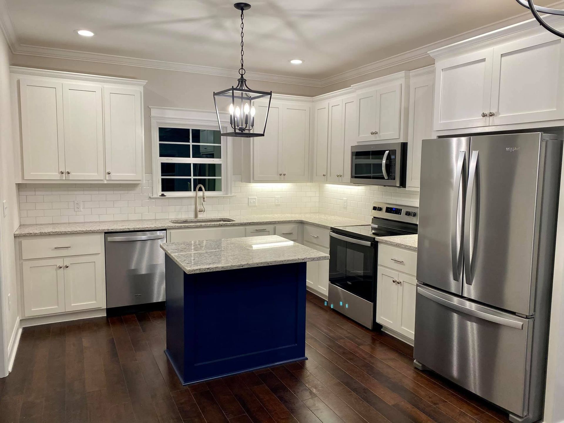 Kitchen with white cabinets, stainless steel appliances, and a blue island with granite countertop.