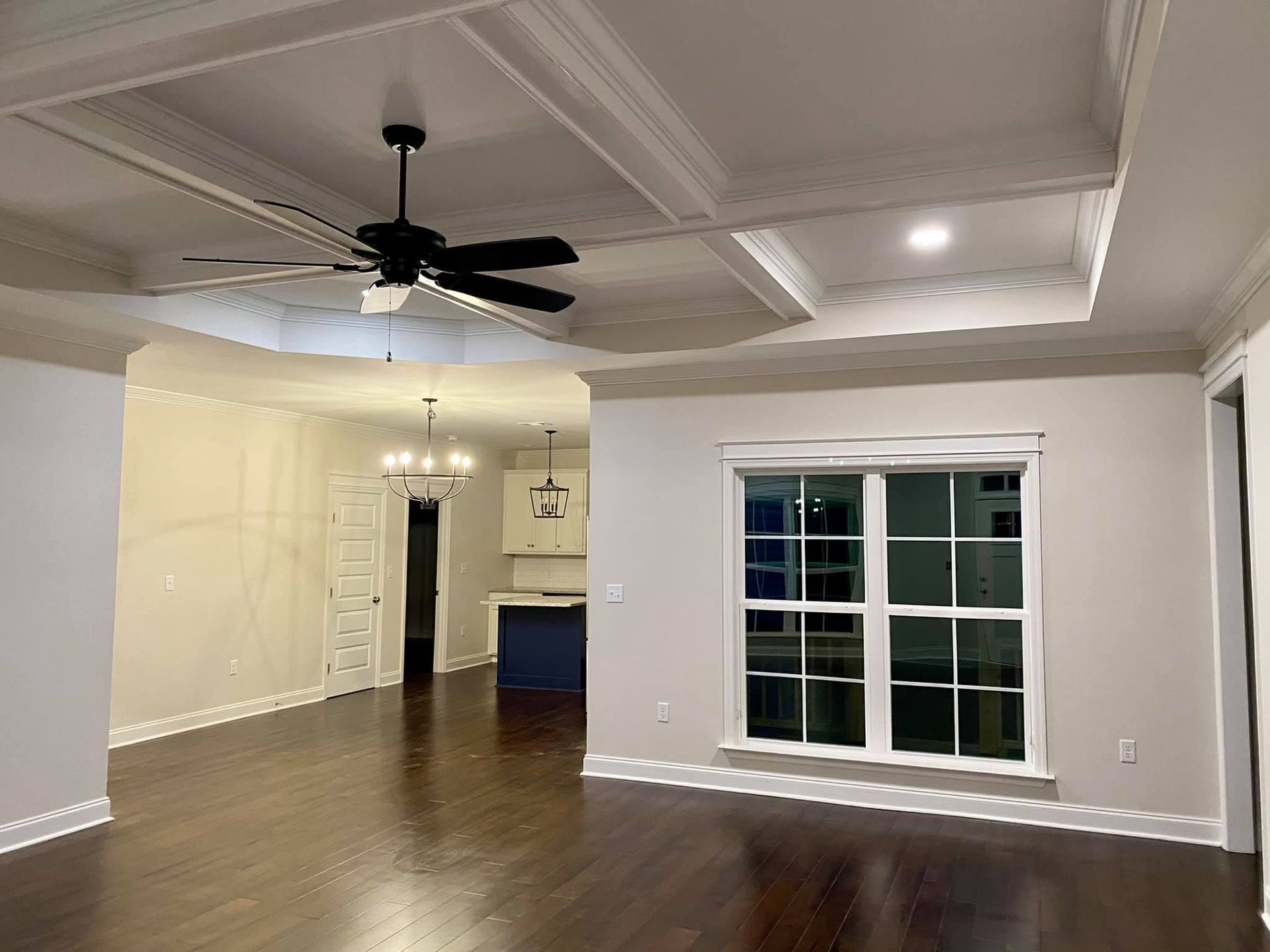 Living room with dark wood floor, coffered ceiling, ceiling fan, and window.