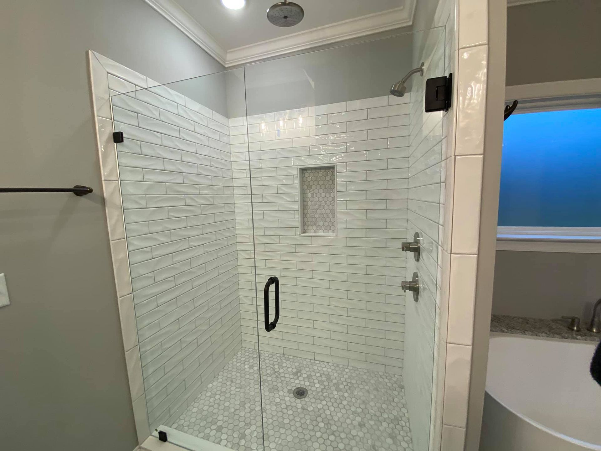 Glass-enclosed shower with white textured tile walls, pebble floor, and black hardware in a bathroom setting.