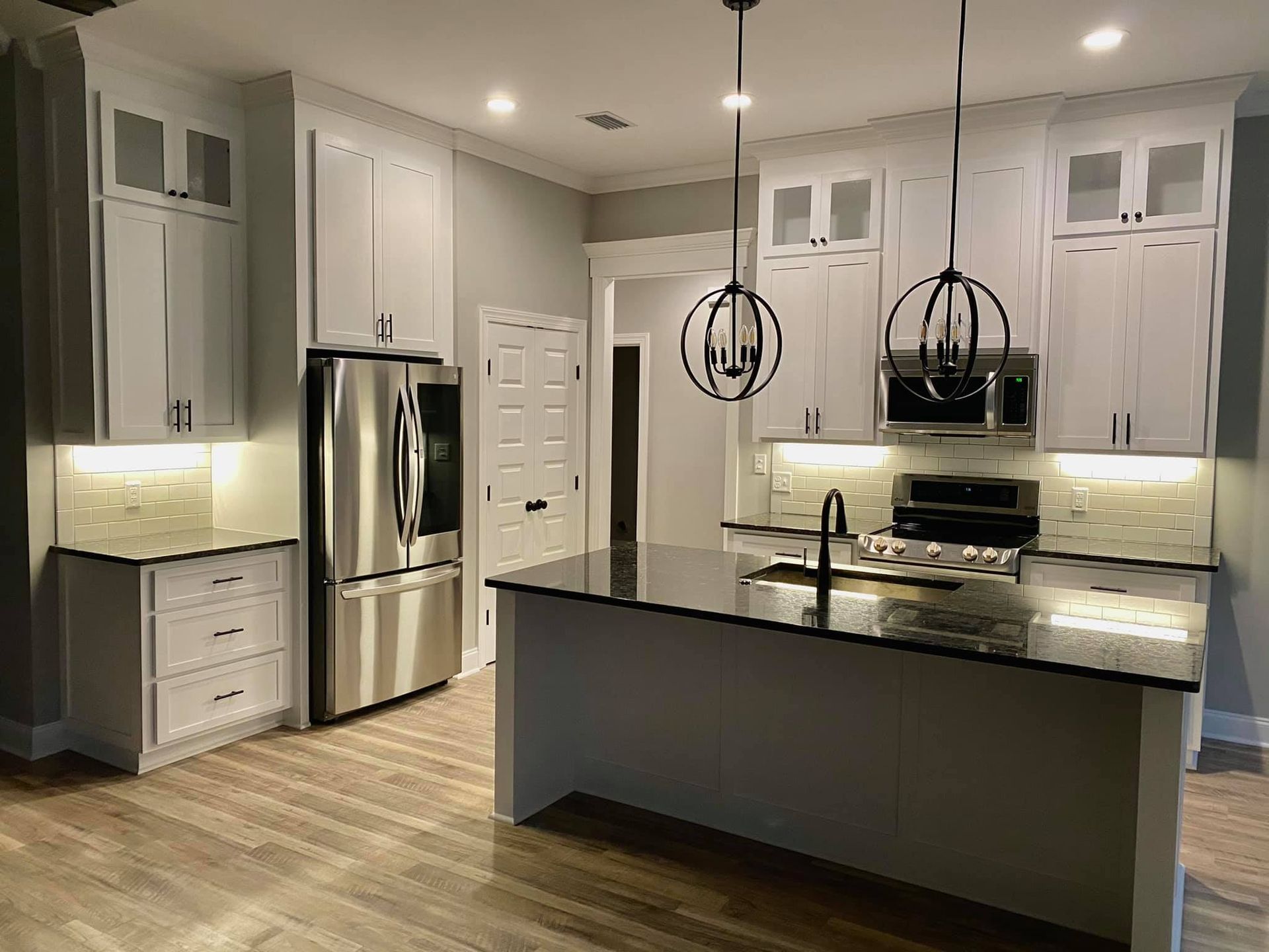 Modern kitchen with white cabinets, stainless steel appliances, and a black countertop island.