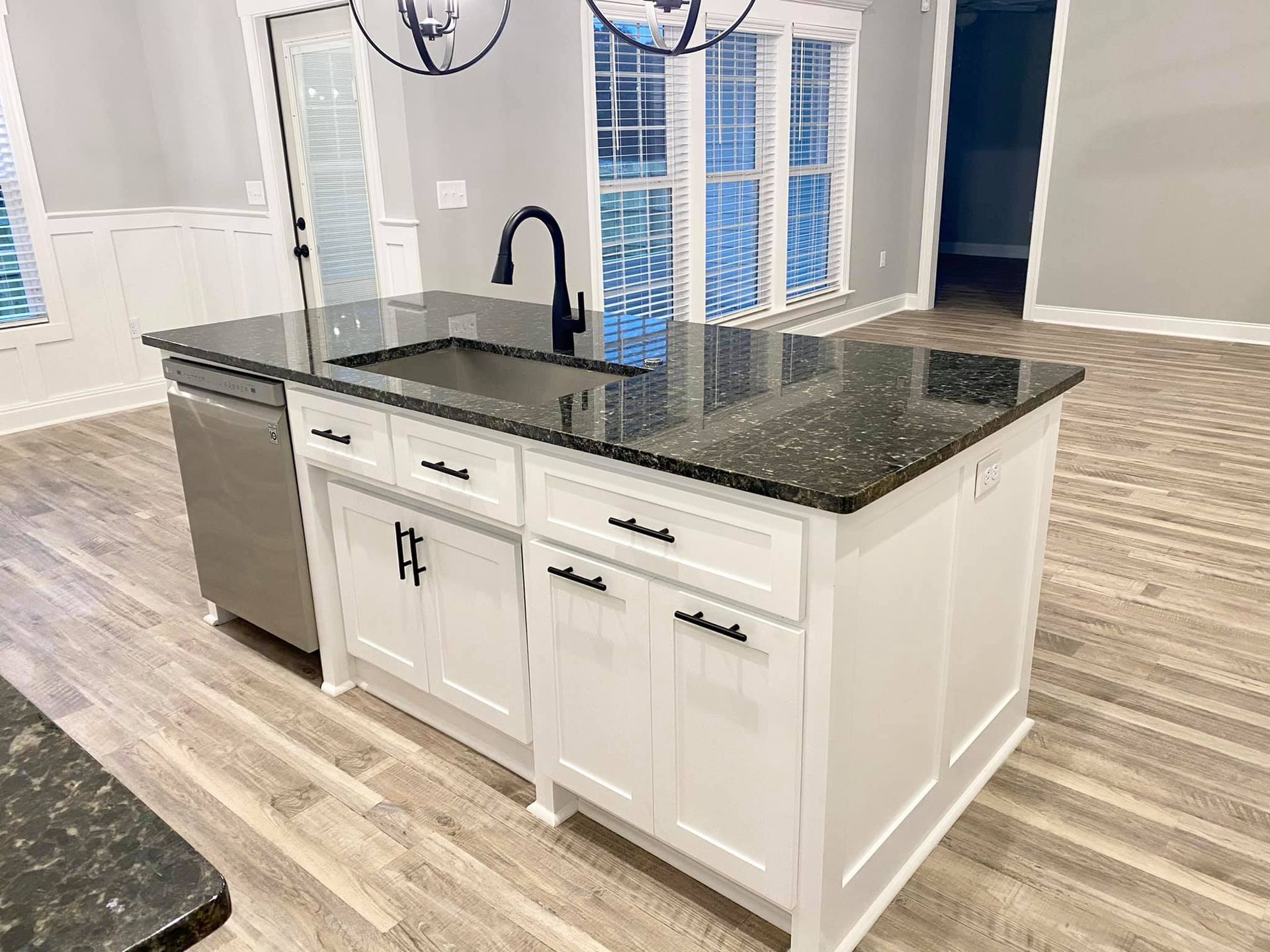 Kitchen island with white cabinets, dark countertop, sink, and black faucet.