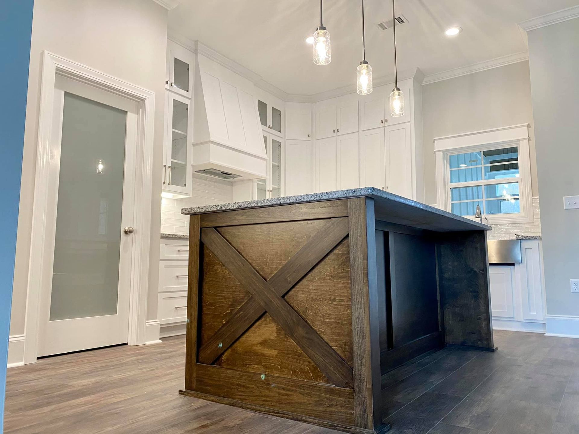 Kitchen with a stained wood island with an X design, white cabinets, and pendant lights.