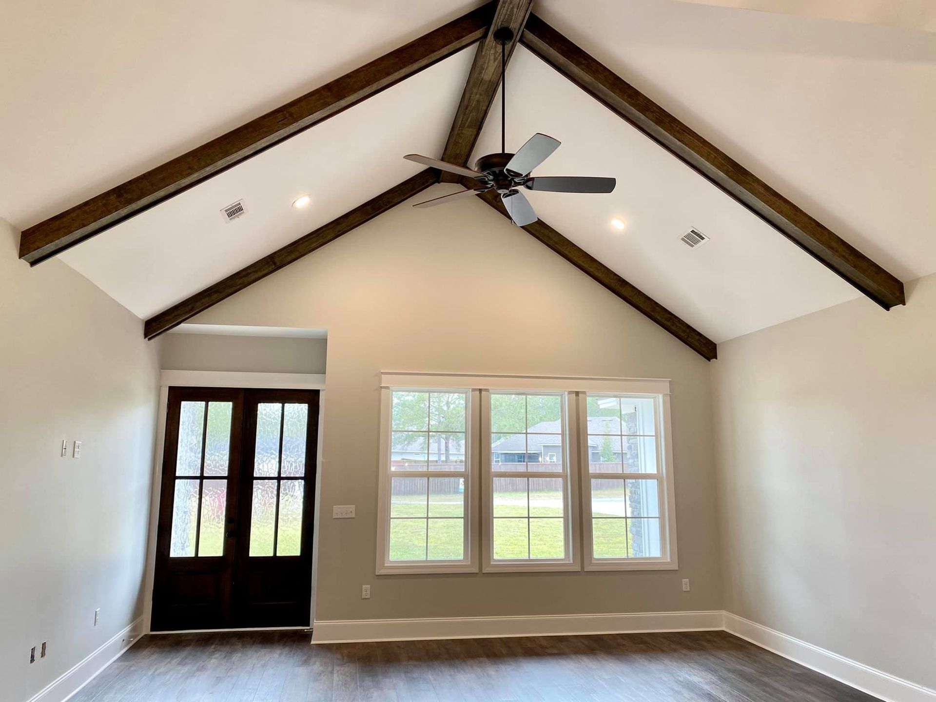Vaulted ceiling living room with wooden beams, dark door, and windows.