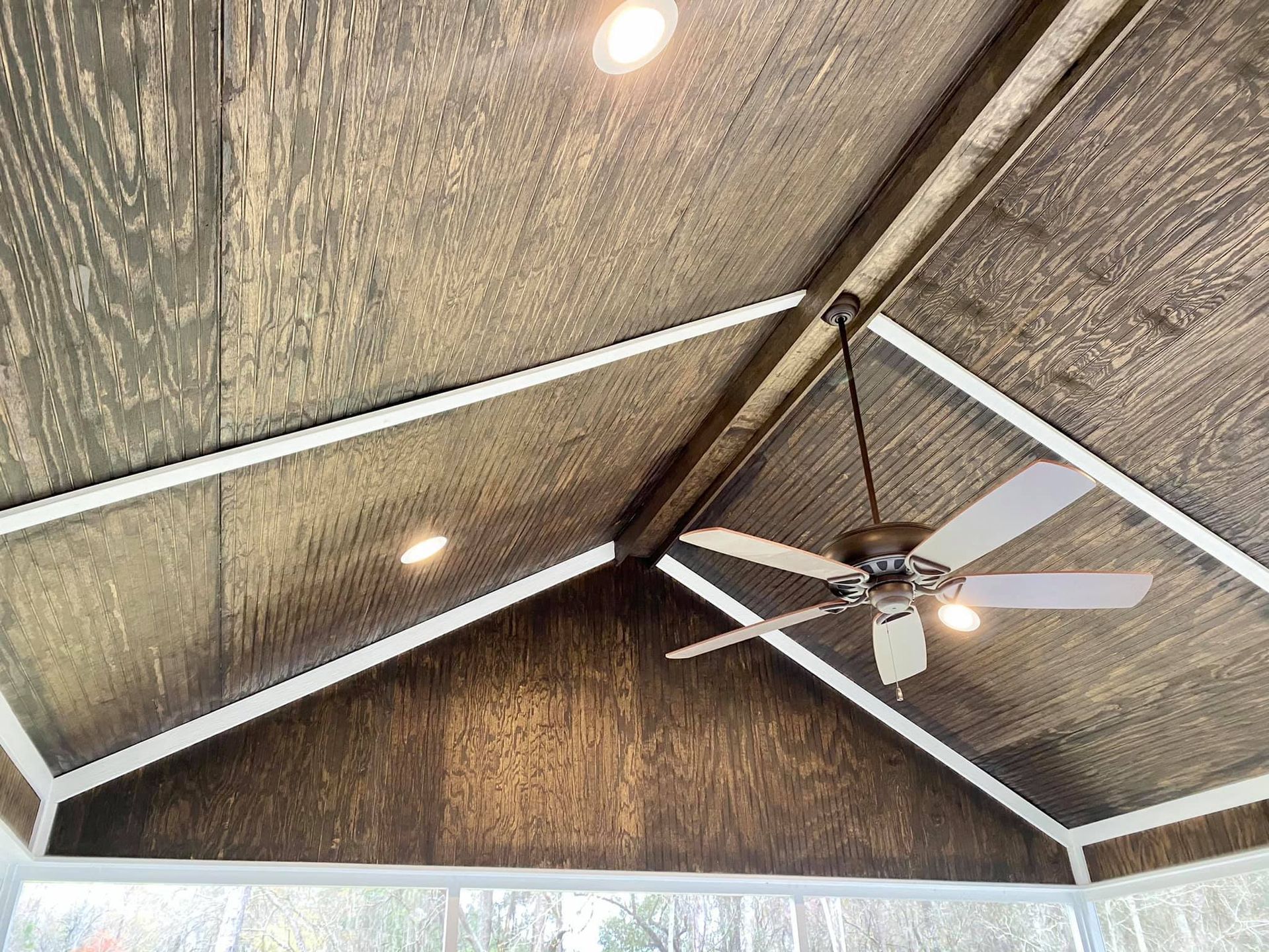 Angled wooden ceiling with recessed lights, ceiling fan, and white trim.