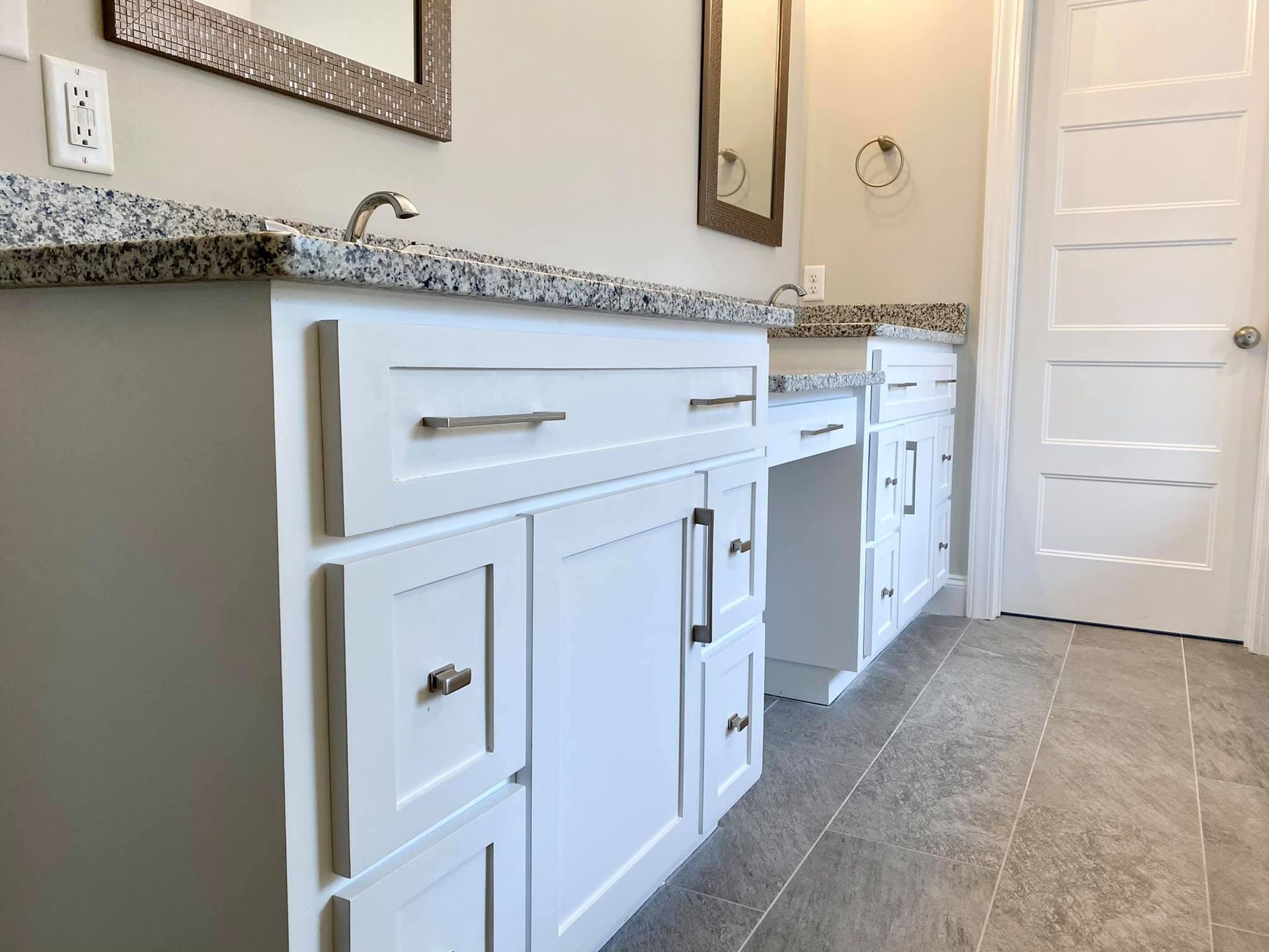 White bathroom vanity with granite countertop, sinks, and a white door.