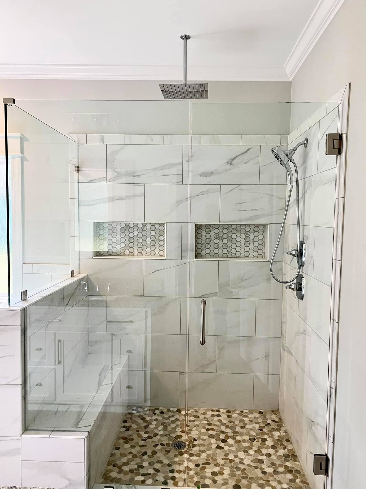 Glass-enclosed shower with white marble tile, pebble floor, and rain showerhead.