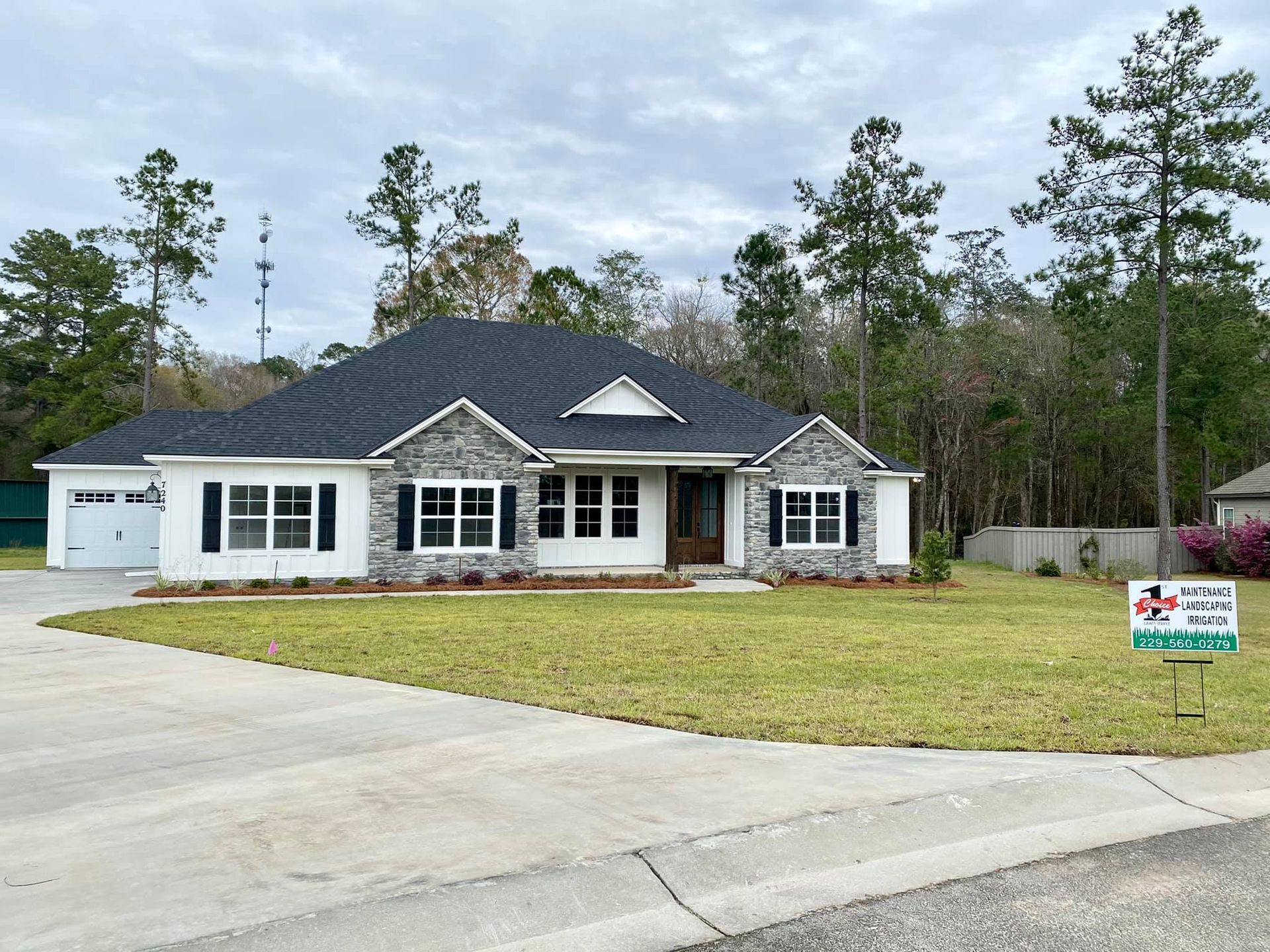 White house with gray stone accents and dark roof, set on a green lawn with trees in the background.