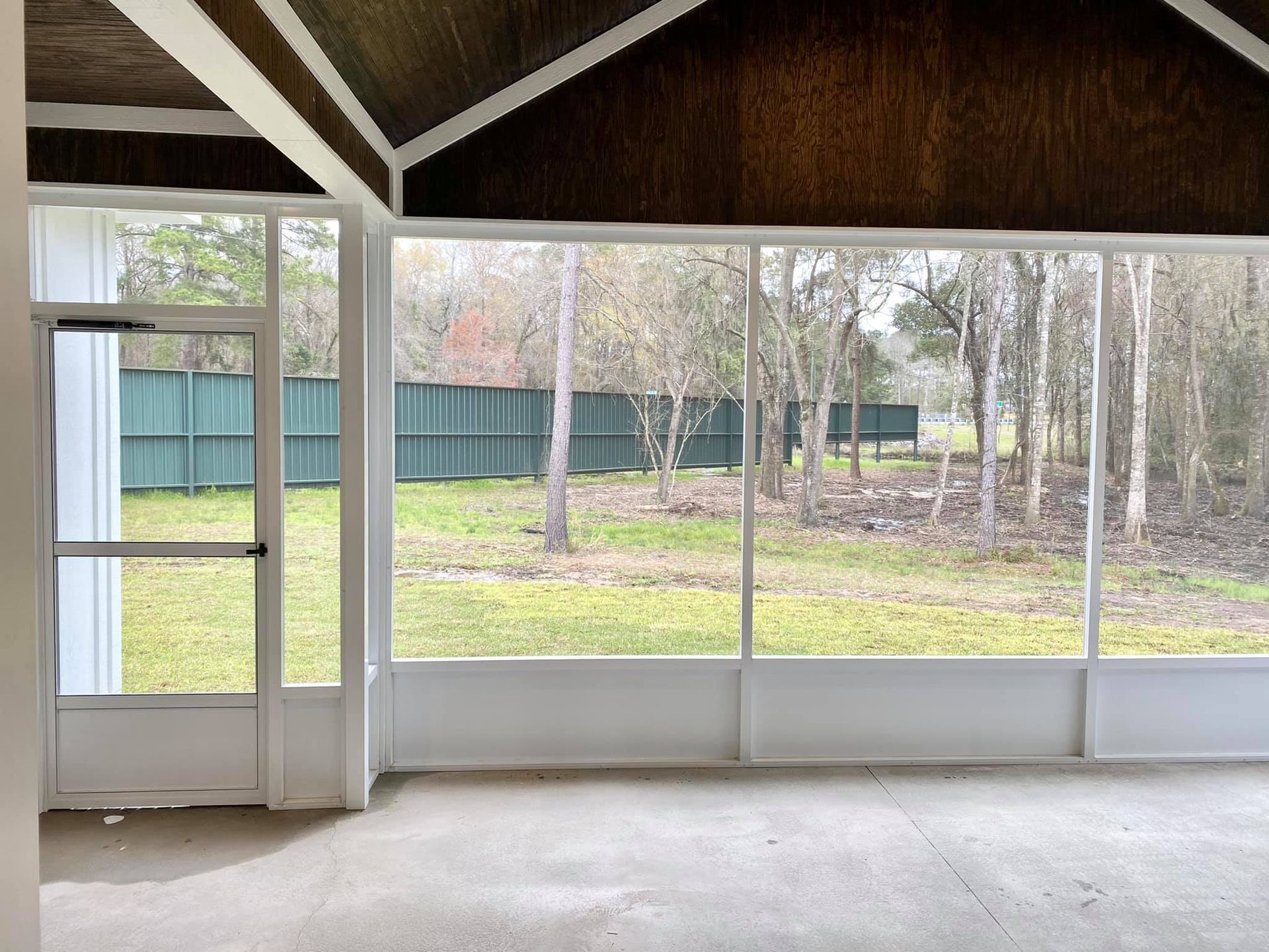 Screened-in porch with view of backyard, green grass, trees, and a green fence.