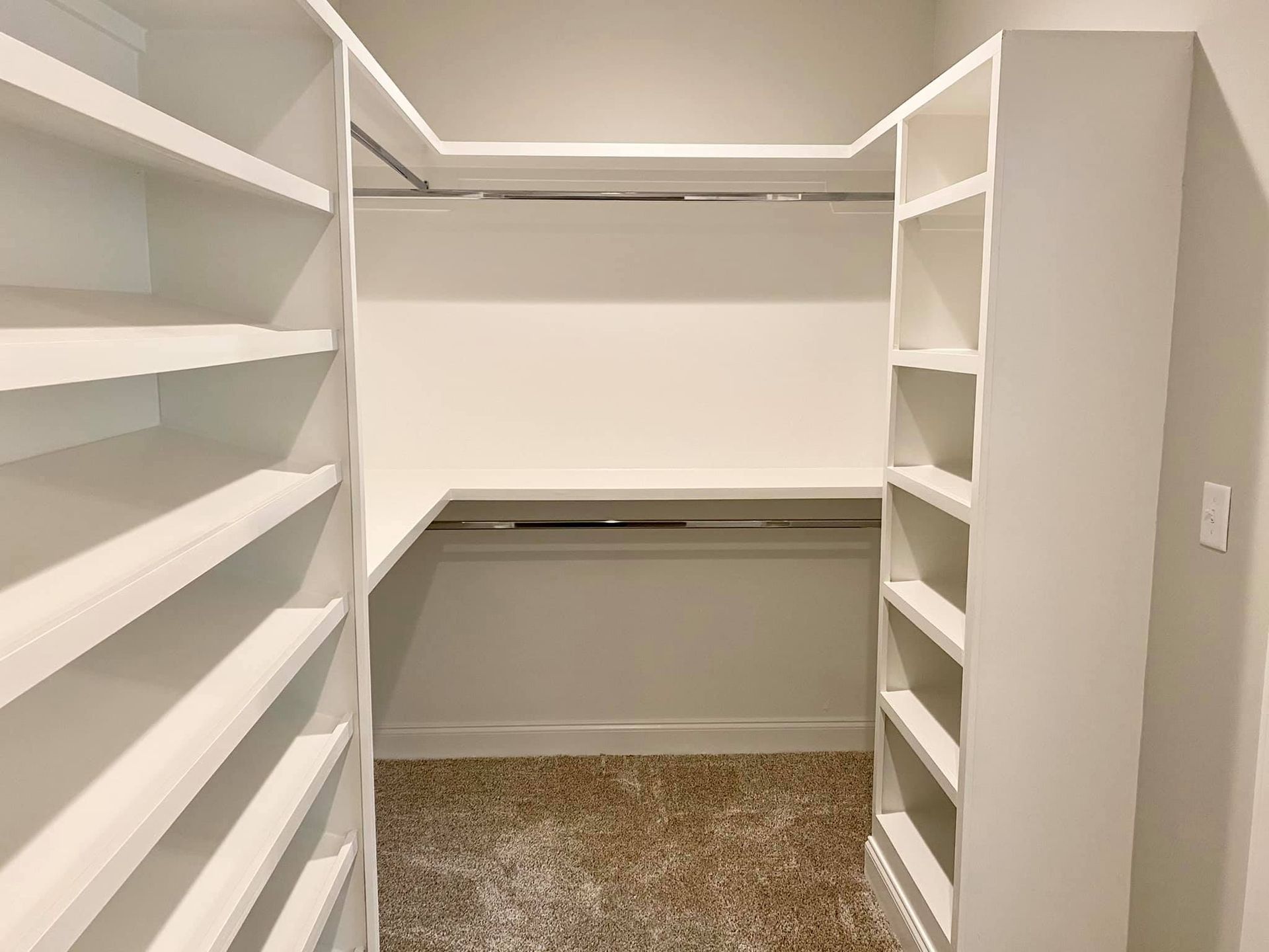 Empty, built-in white closet with shelving, a rod, and beige carpet.