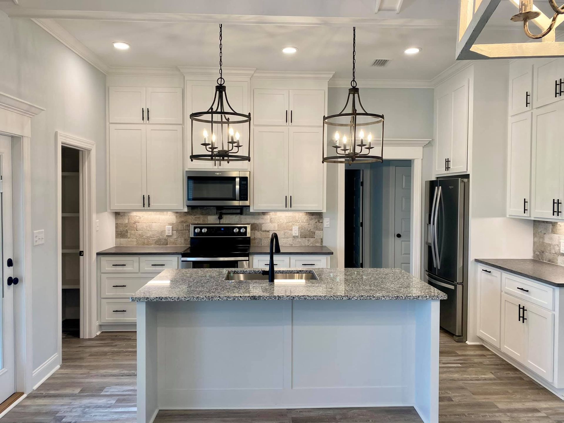 White kitchen with island, cabinets, granite countertops, and black light fixtures.