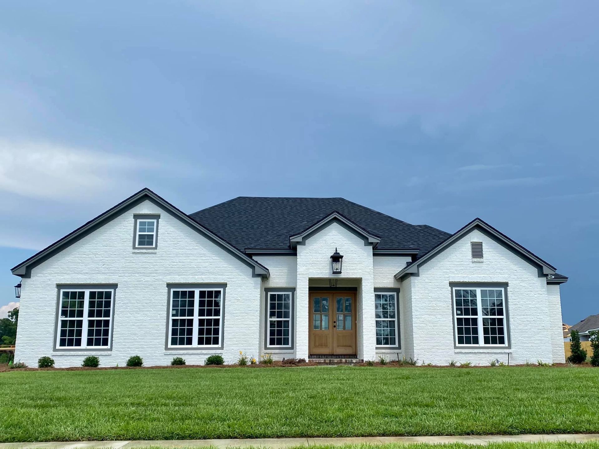 White brick house with black trim and dark roof under a cloudy sky.