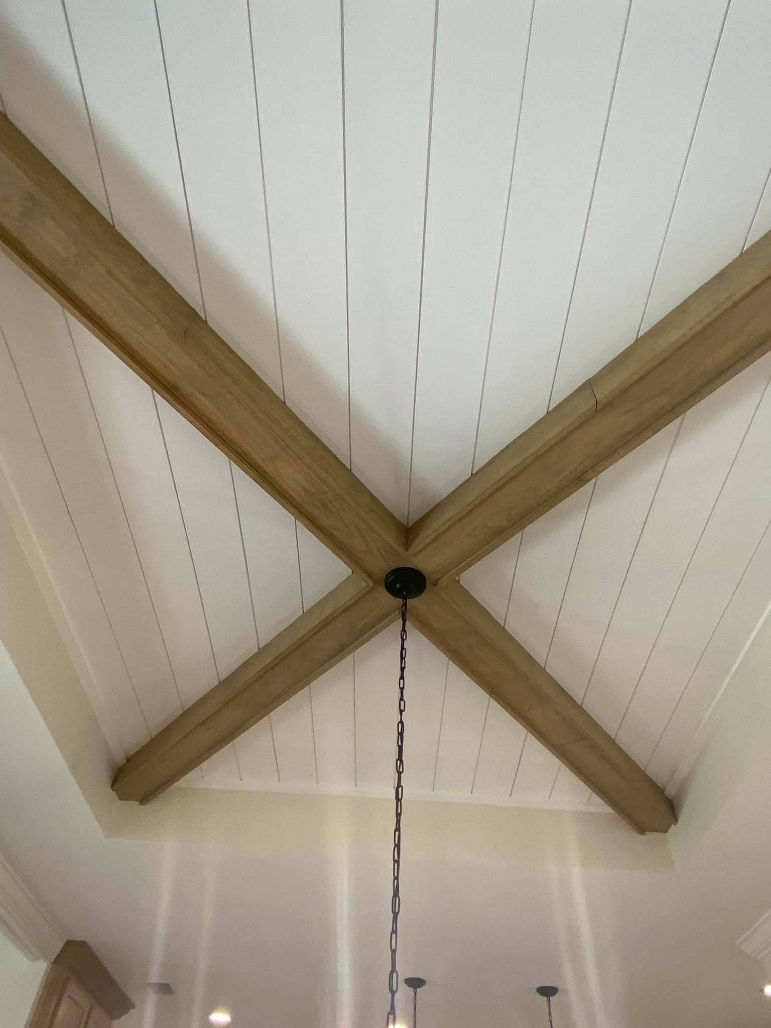 Wooden beams cross on a white, paneled ceiling; a black light fixture hangs.