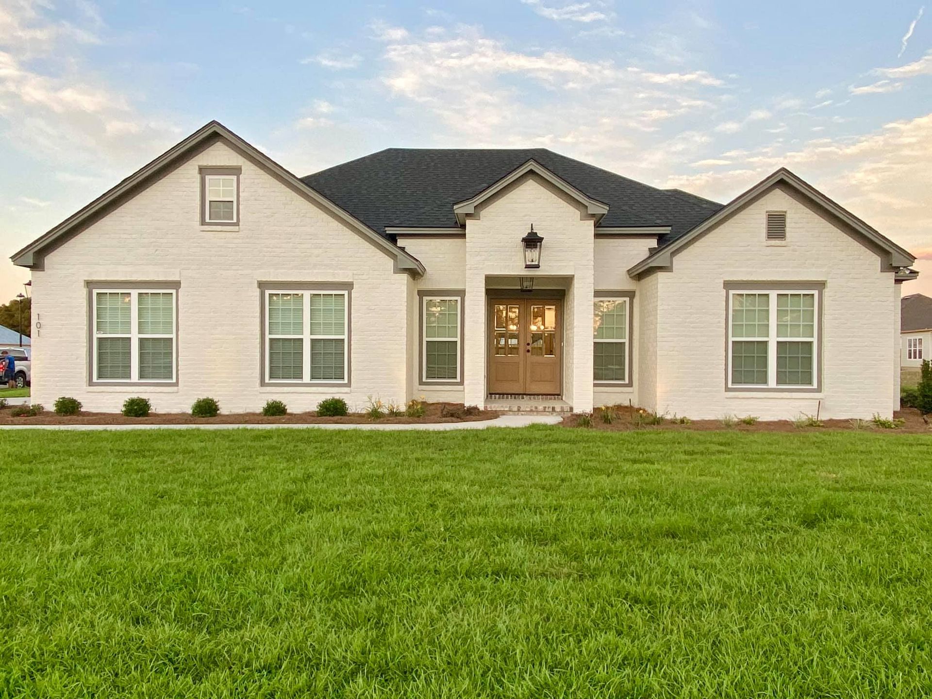 White brick house with dark roof, windows, and green lawn.