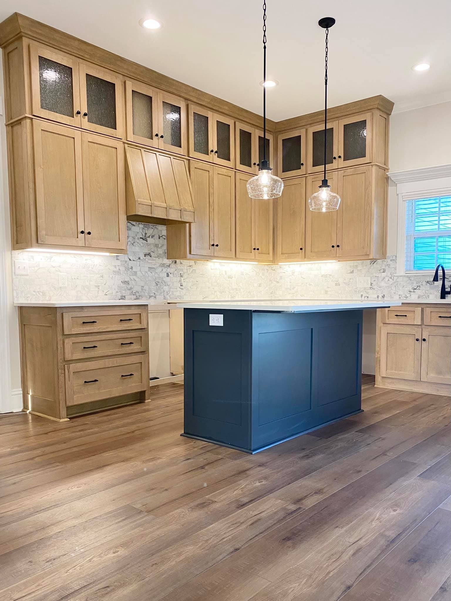 Kitchen with light wood cabinets, dark blue island, white countertops, and wood floor.