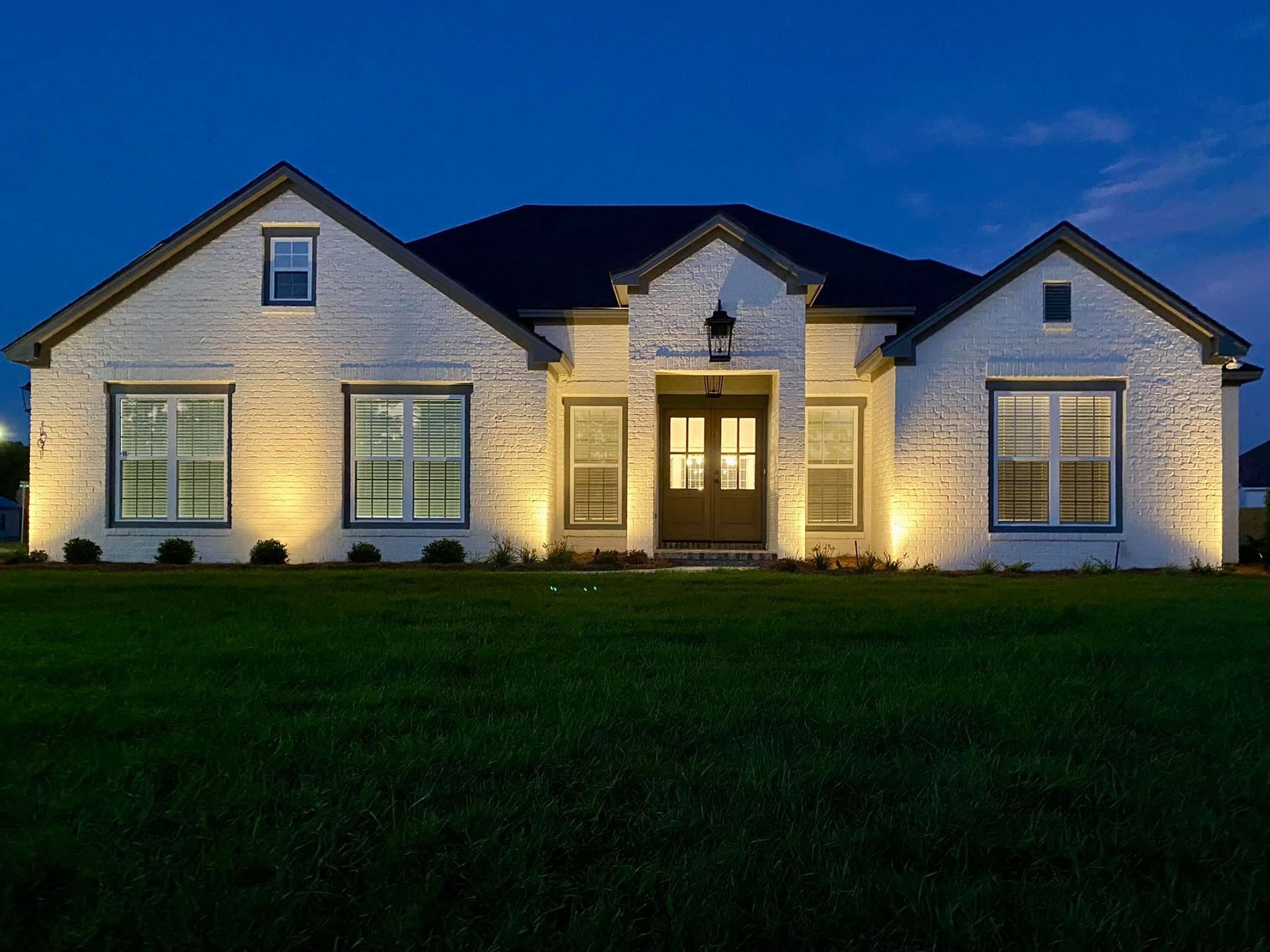 White brick house with outdoor lights, set against a twilight sky.