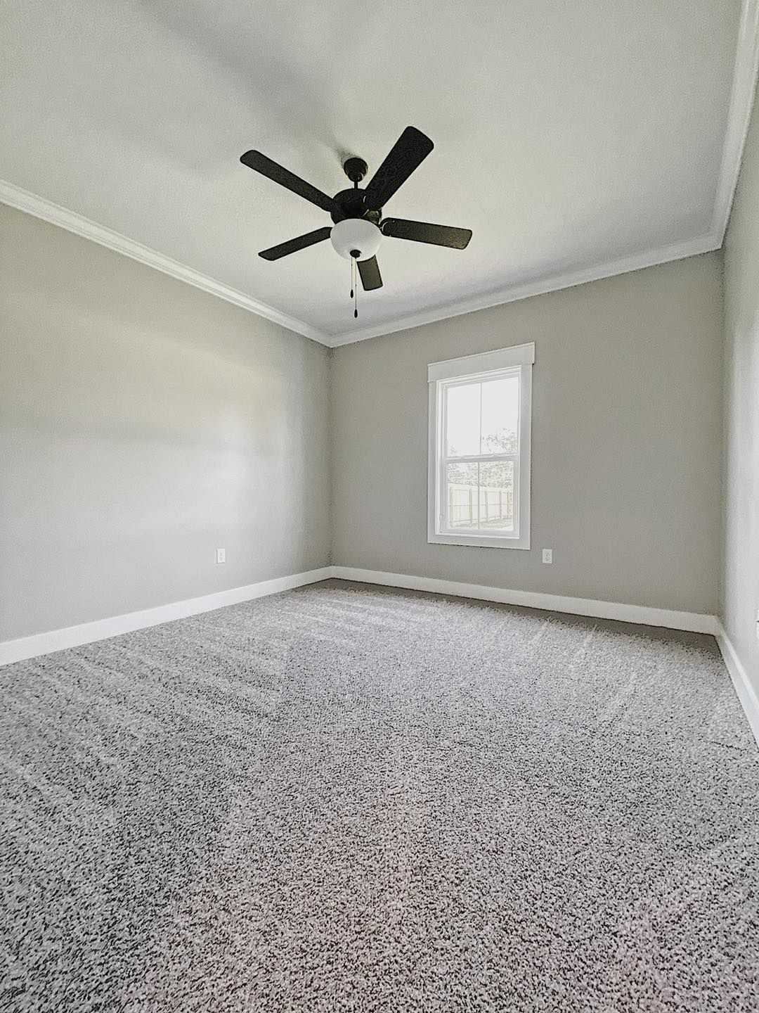 Empty room with gray carpet, walls, and ceiling, featuring a ceiling fan and a window.