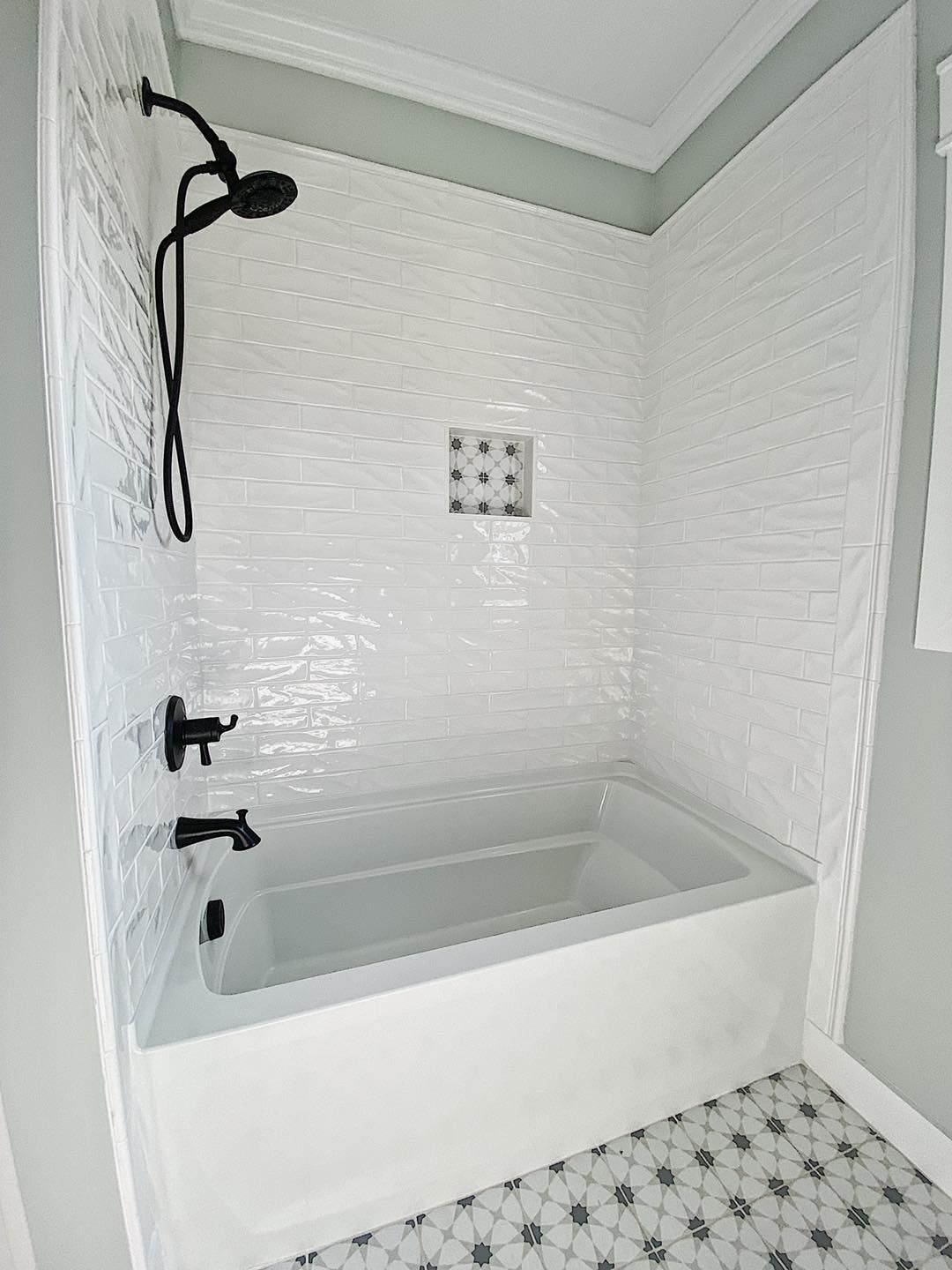 White tiled shower with black fixtures and a bathtub. Black and white patterned floor.