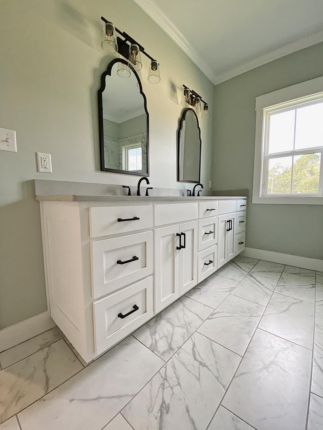 White bathroom vanity with two mirrors, black hardware, and marble-look tile flooring.