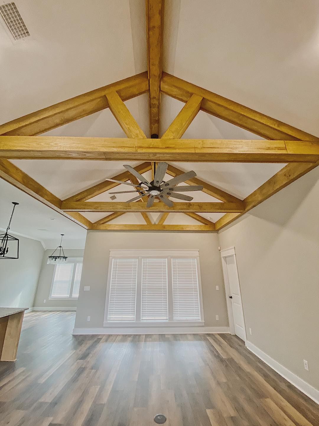 Living room with wooden beams on the high ceiling, shuttered windows, and a ceiling fan.
