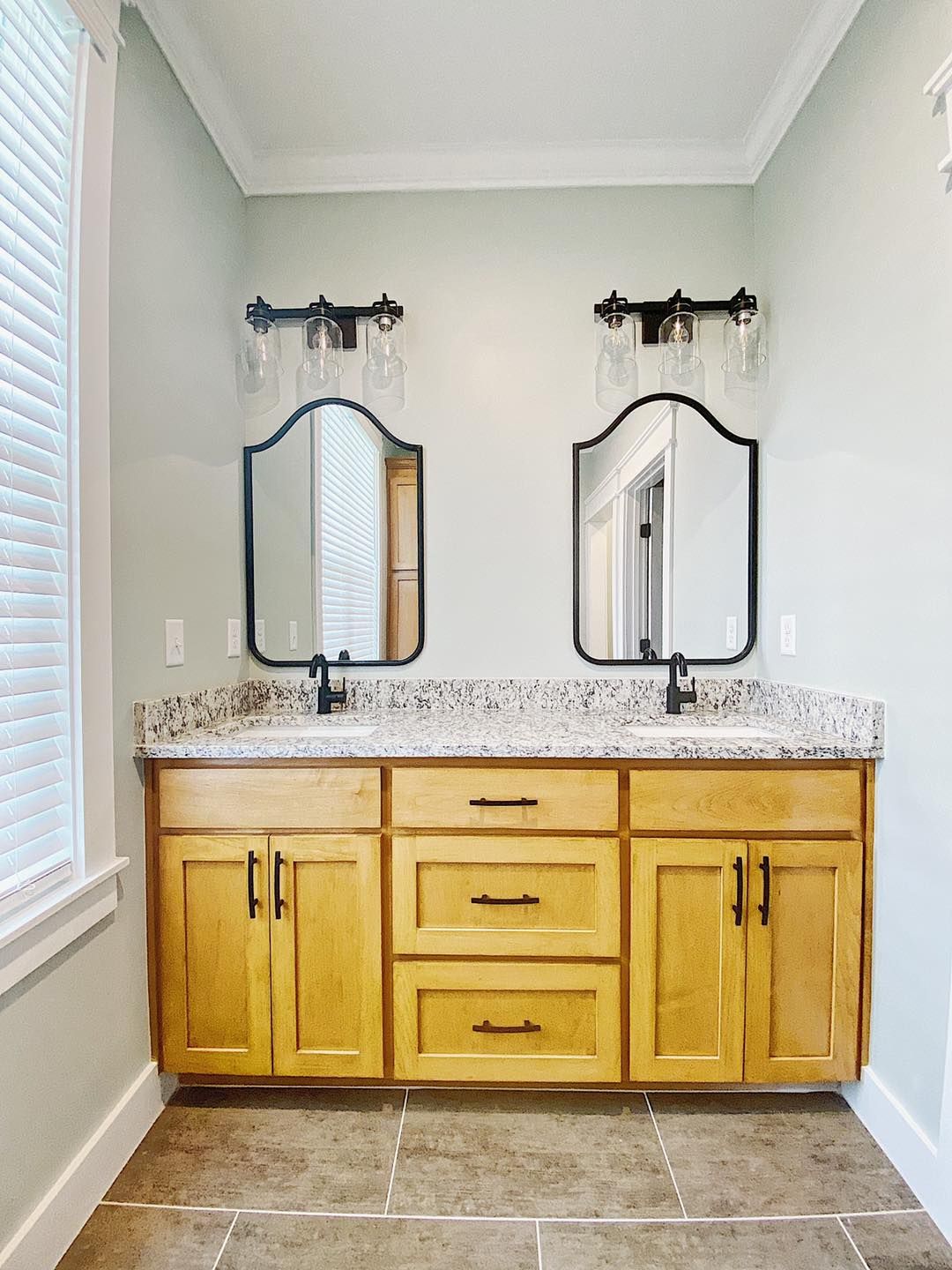 Bathroom with dual sinks, mirrors, and cabinetry. Beige countertop and light wood cabinets, mirrors with black frames.
