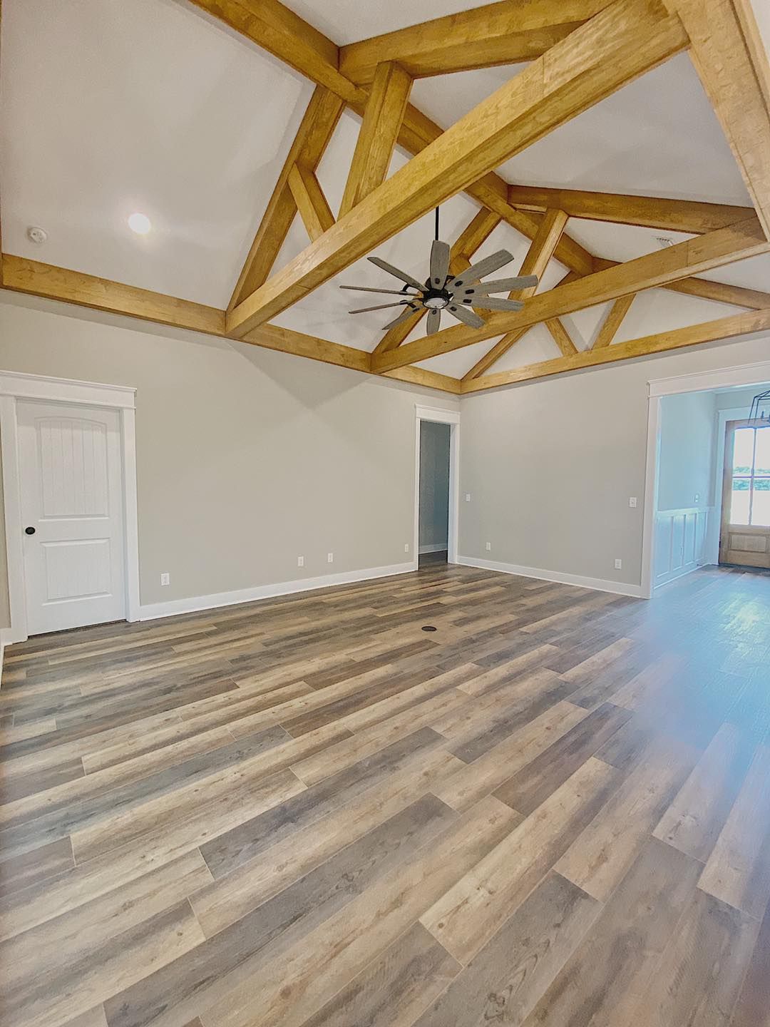 Empty living room with wood flooring, light gray walls, and exposed wooden beams on the ceiling.