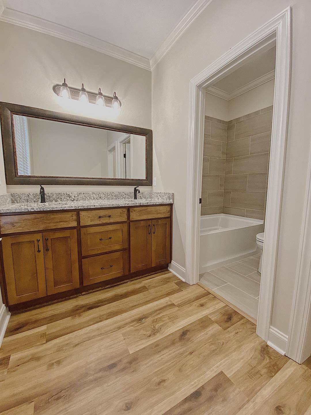 Bathroom with wooden vanity, large mirror, and open doorway to a shower/bathtub area. Light brown flooring.