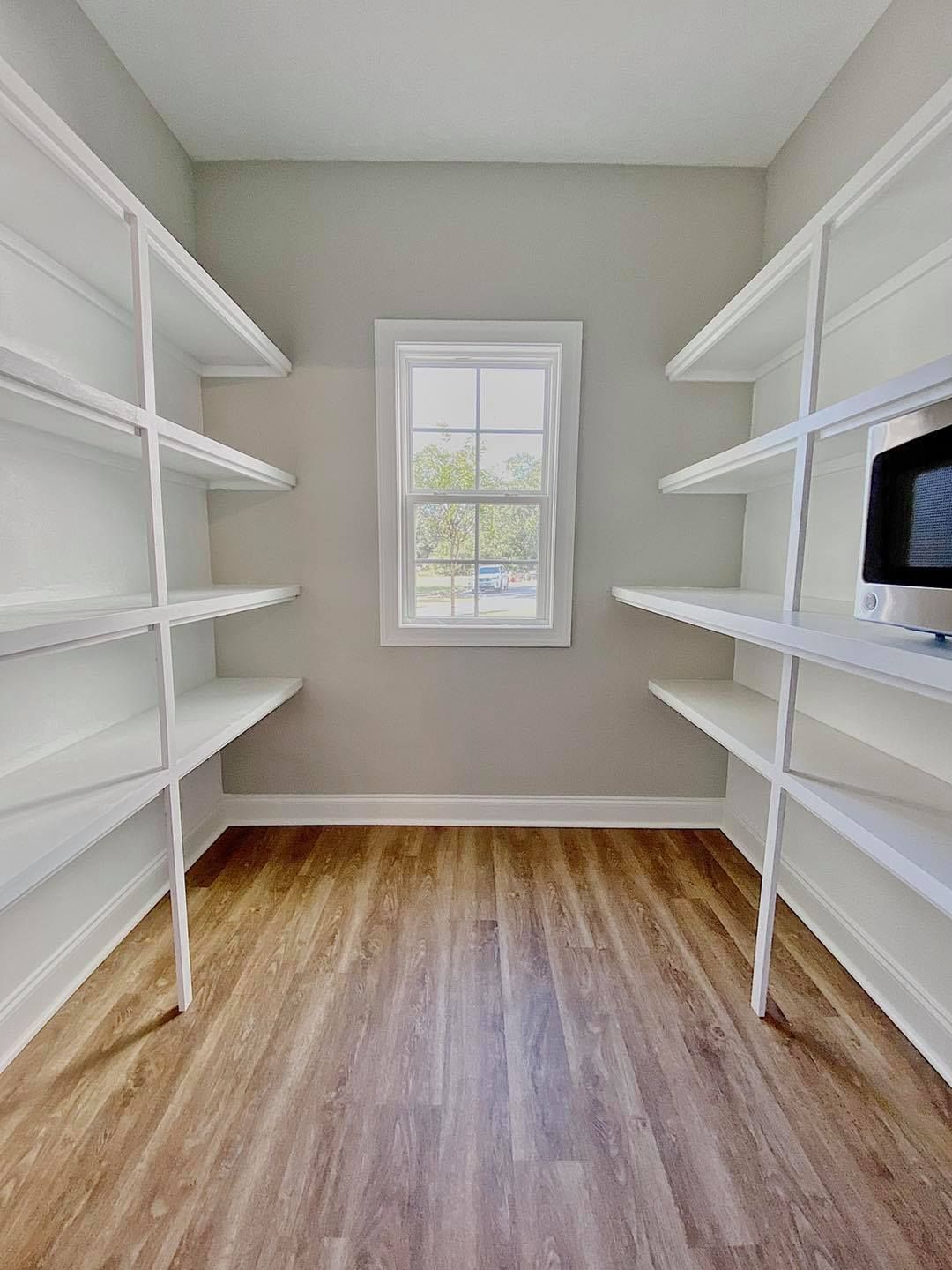 Empty pantry with white shelving, a window, and wood-look flooring.