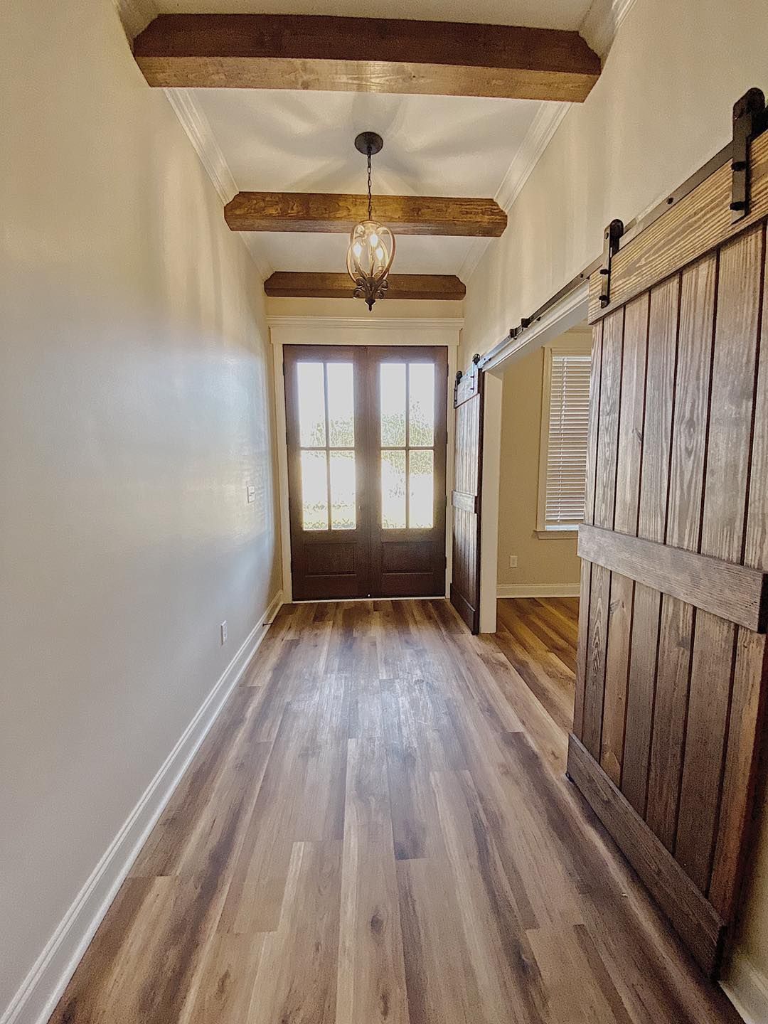 Hallway with wooden beams, flooring, and sliding door. Front door visible at end.