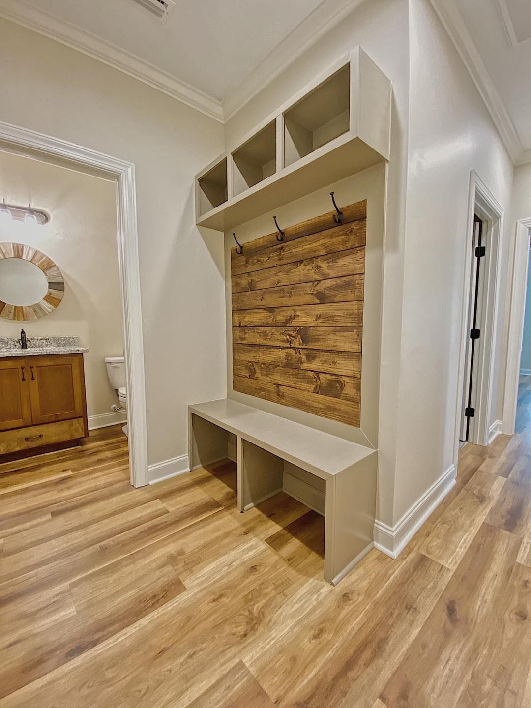 Hallway with wooden floor, built-in mudroom bench, shelves, and wood-paneled backing with hooks. Beige walls and doorway.