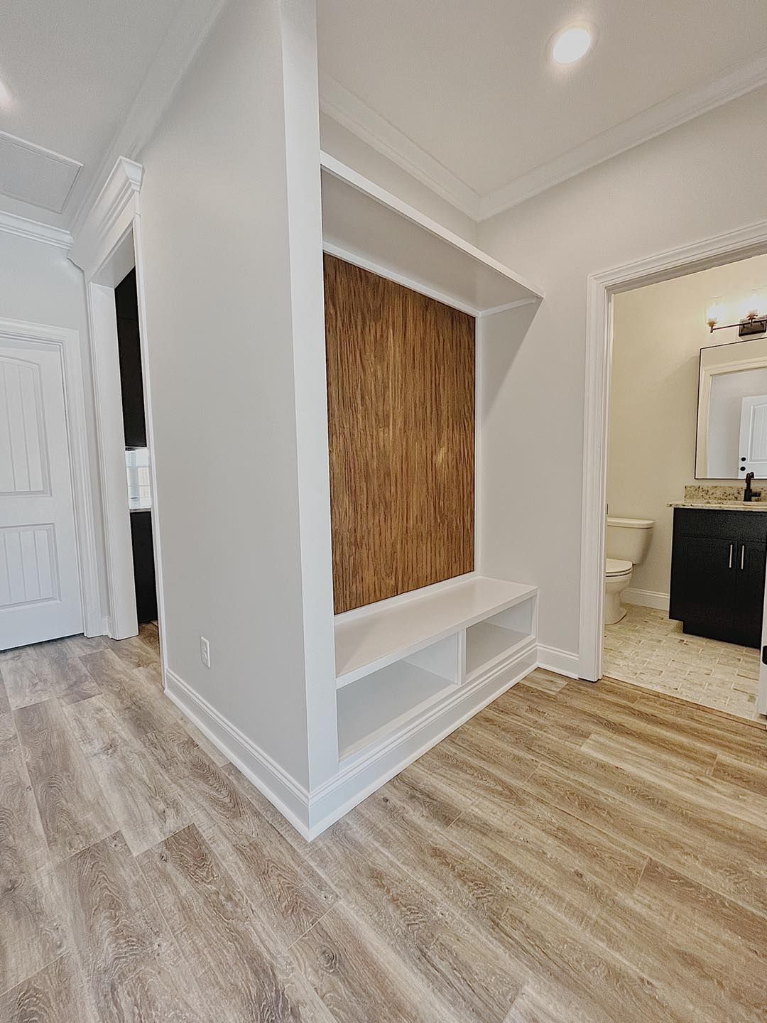 Hallway with built-in bench and storage unit featuring a wood-paneled accent. Light gray walls, light wood flooring.