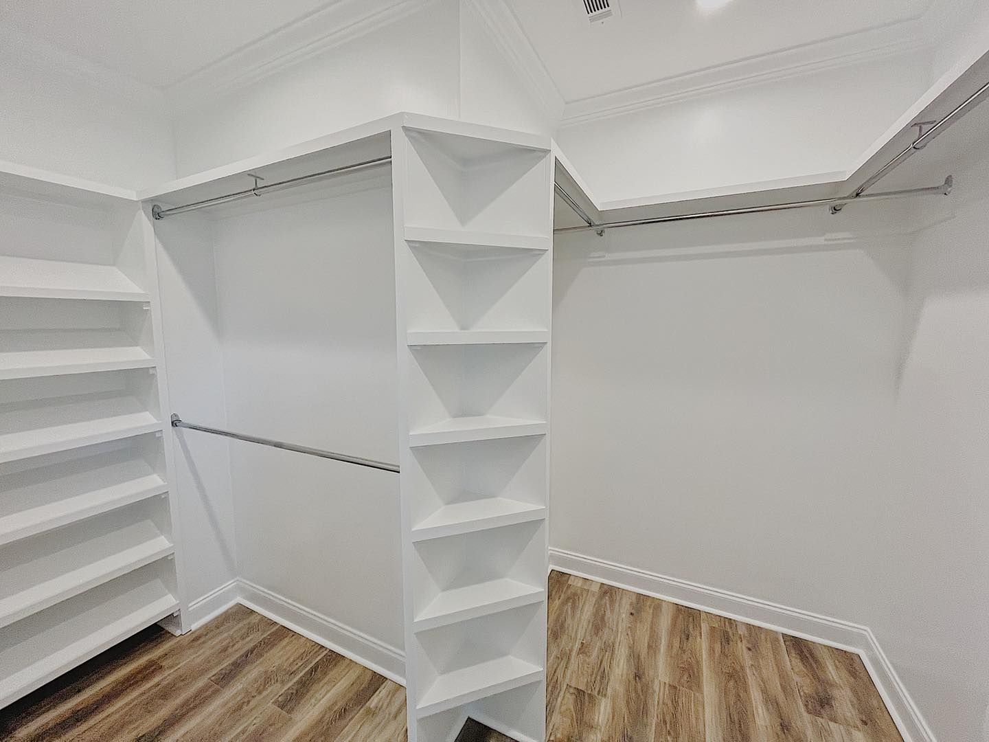 White walk-in closet with shelves and rods, corner shelves, and wood-look flooring.
