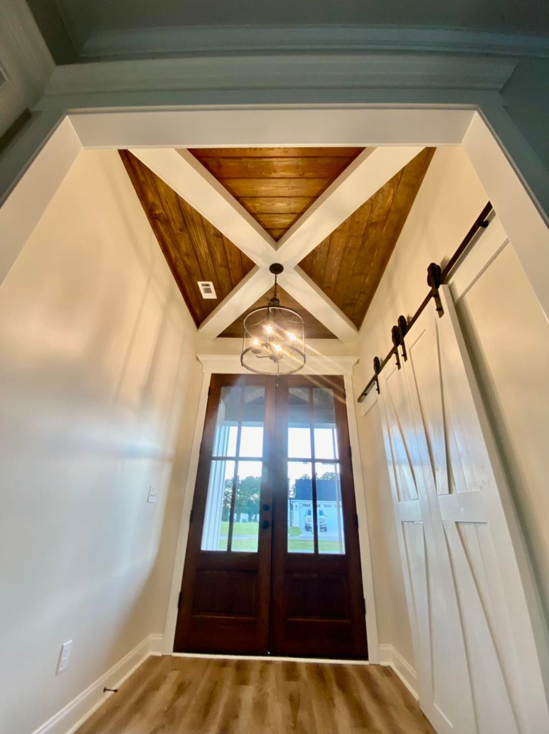 Foyer with wood-paneled ceiling, dark double doors, and white sliding barn door.