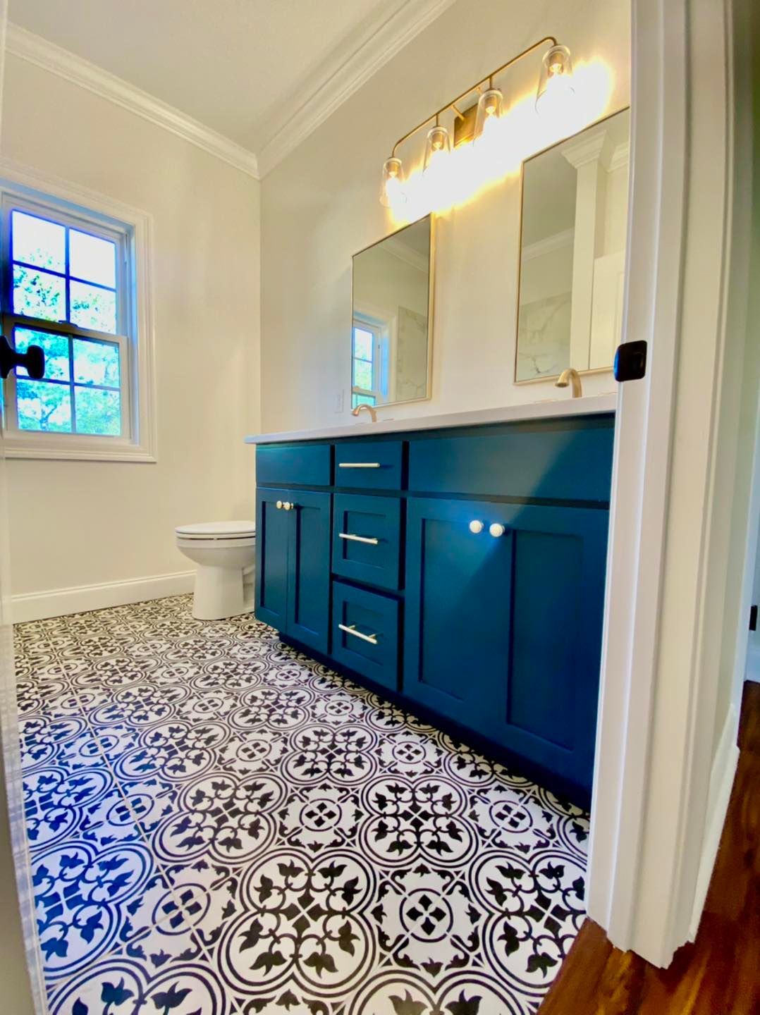 Bathroom with teal vanity, patterned tile floor, and gold-framed mirrors under a light fixture.