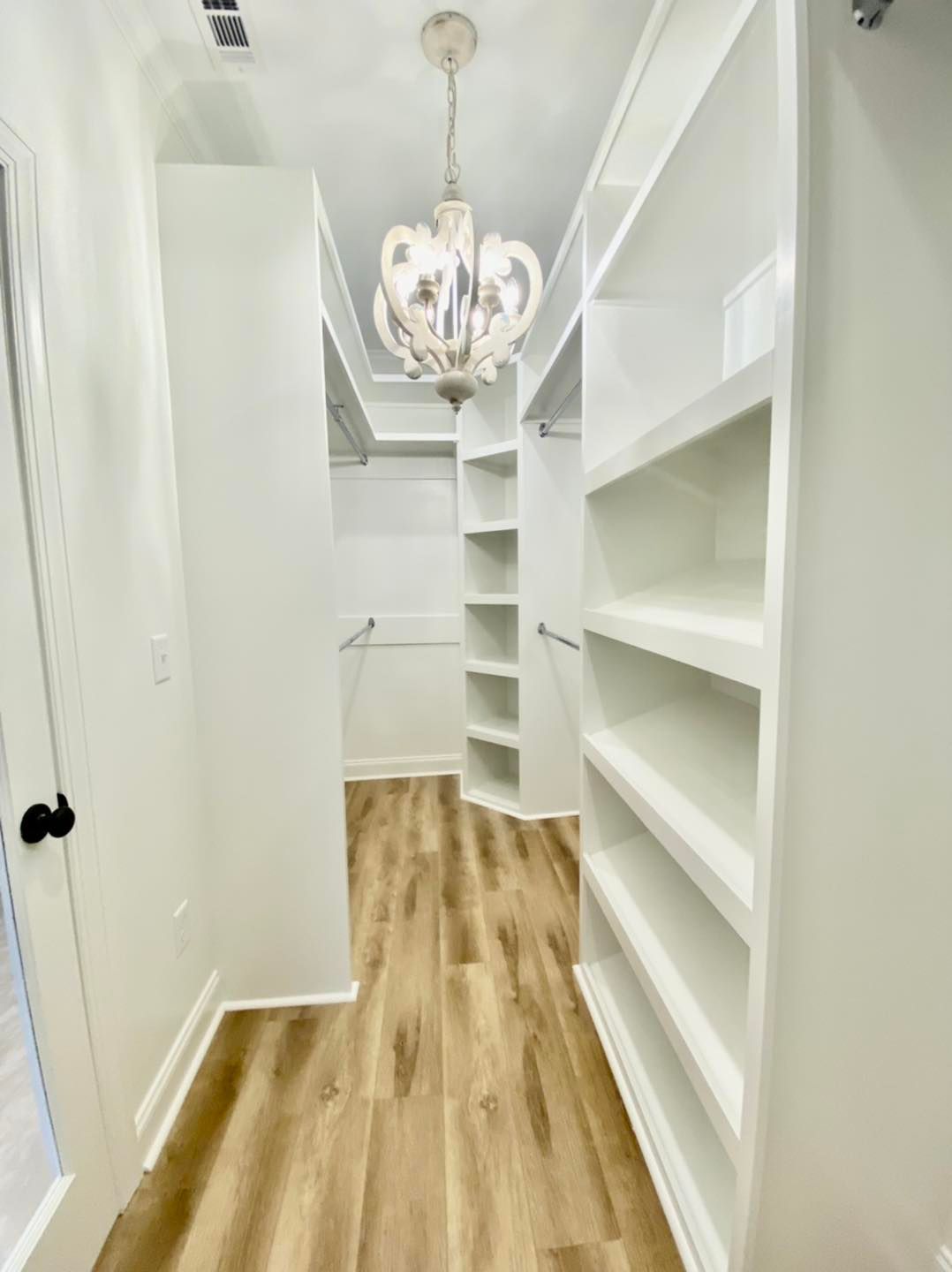 Walk-in closet with white shelves and built-ins, chandelier, hardwood floors.