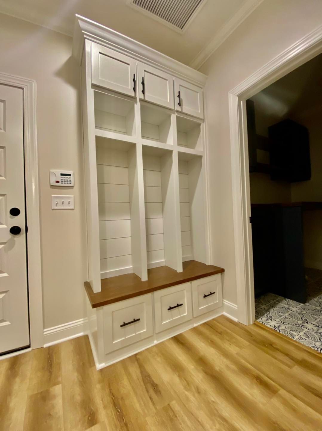 White storage unit with cubbies, cabinets, and bench in a hallway with wood flooring.