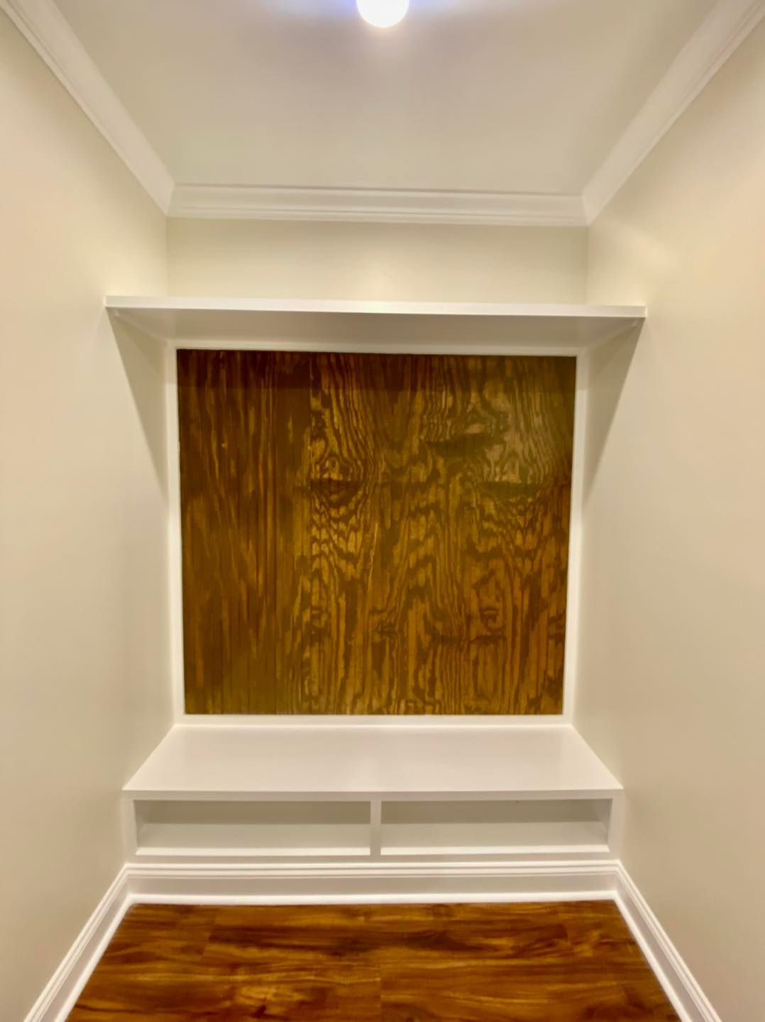 Built-in alcove with wooden backing, white trim, and a shelf. Flooring is wood.