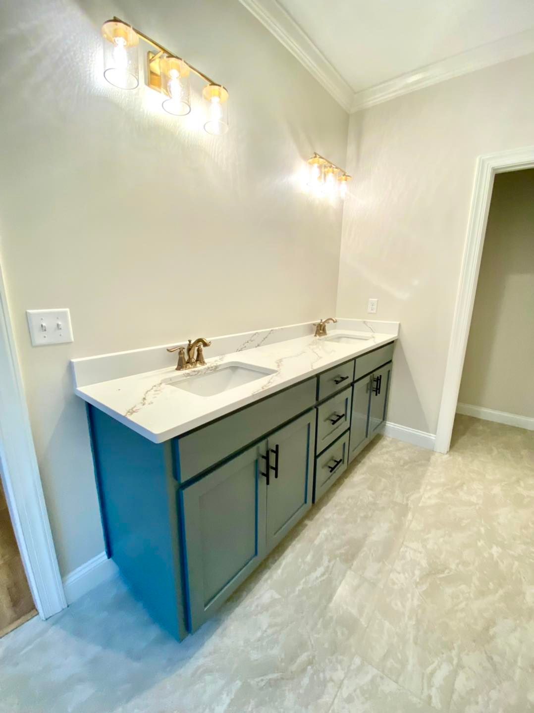 Bathroom vanity with teal cabinets, marble countertop, and gold light fixtures.